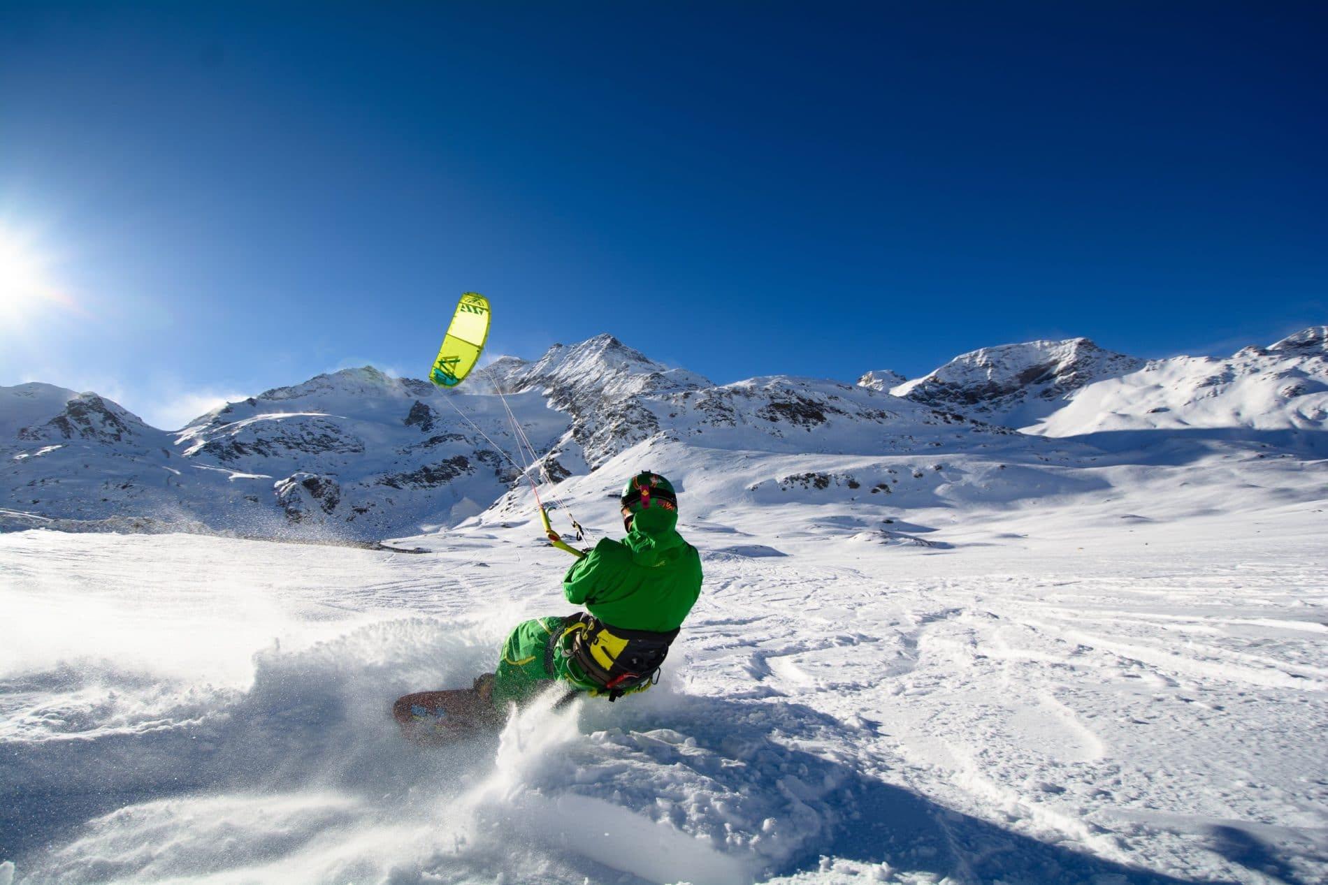 Snowkiter launching off snowy slope with yellow parachute and mountain backdrop