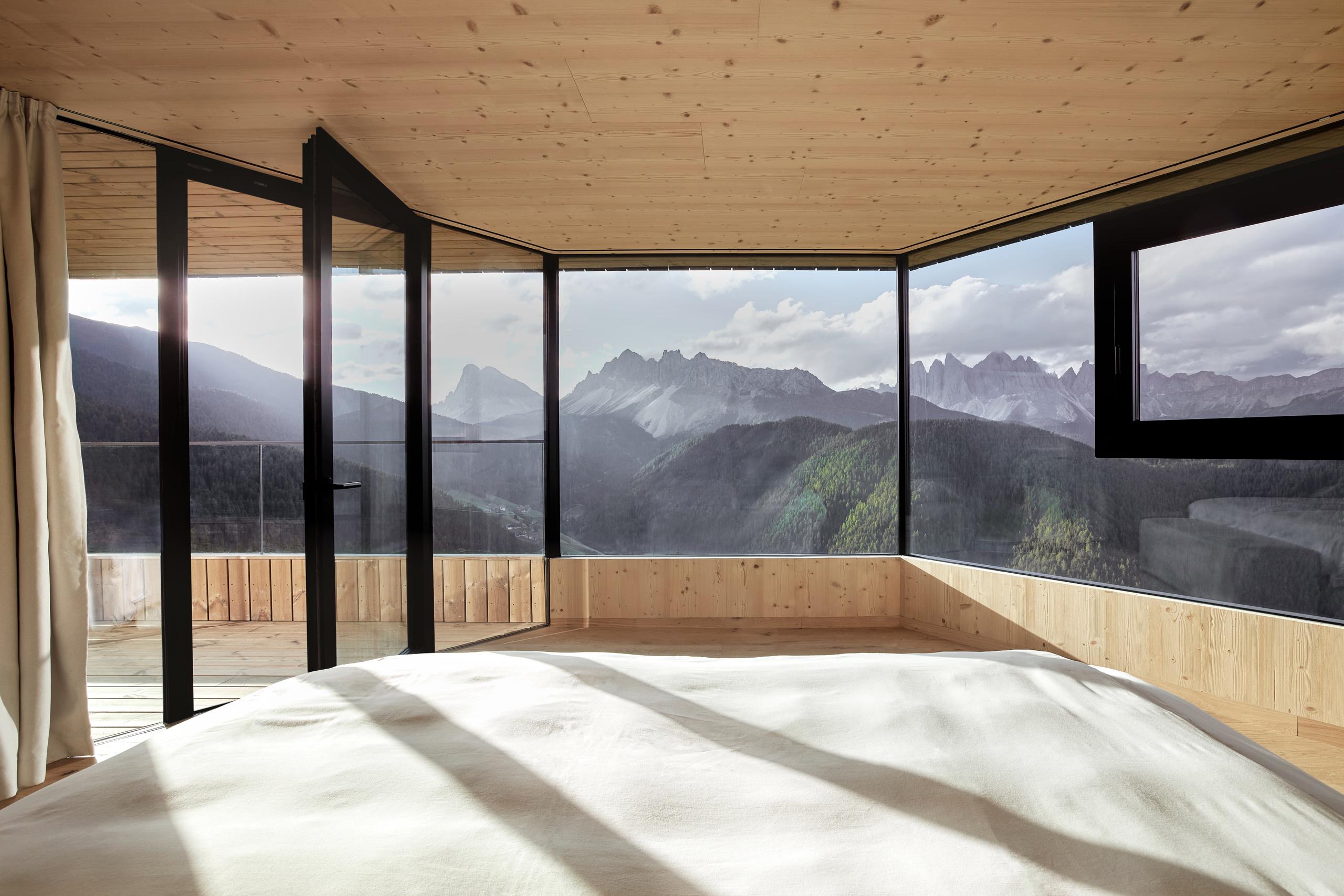 A corner suite with wraparound black-framed windows, light wood finishes, and mountain landscape views