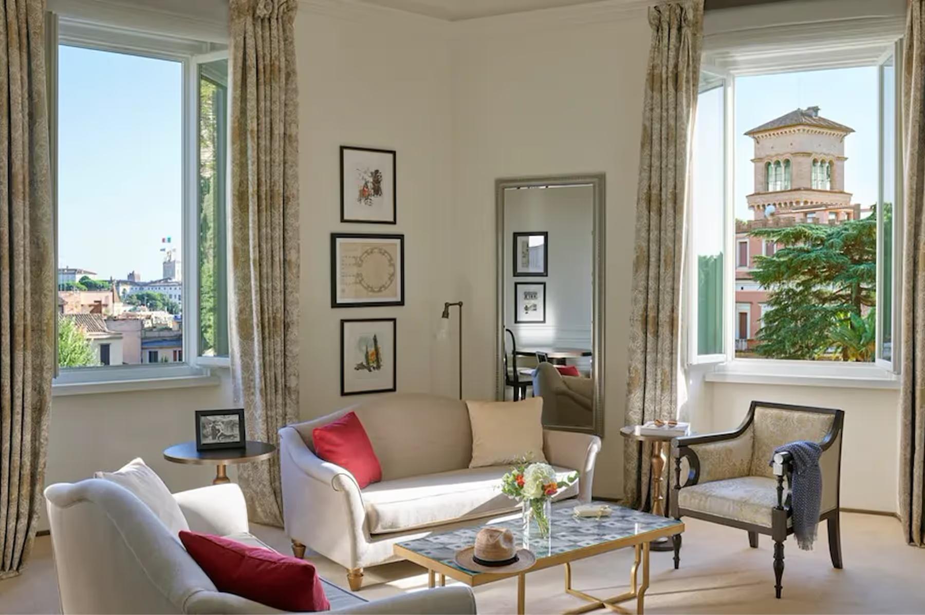 A sitting room with tall windows, beige furnishings, artwork, and panoramic views of Rome’s cityscape