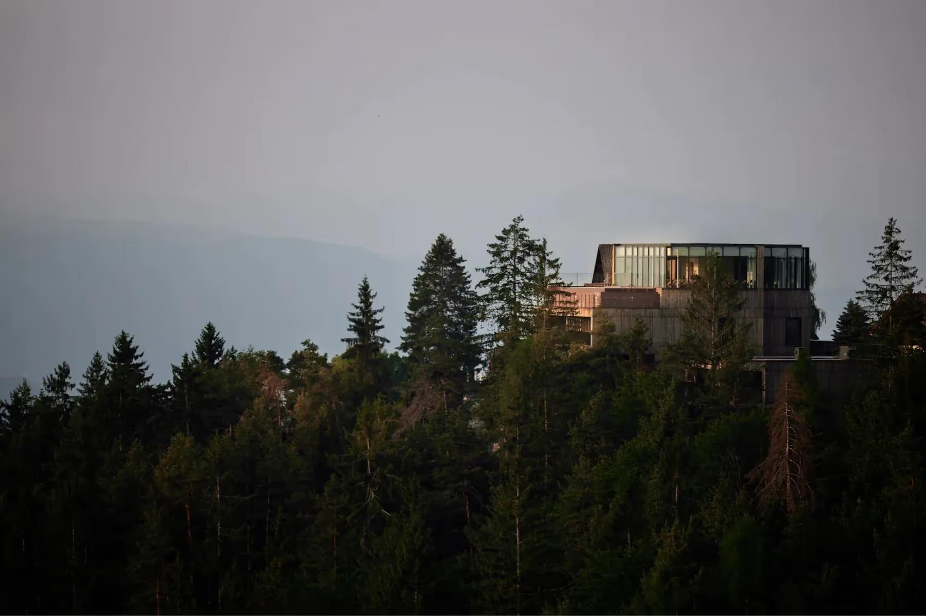Modern wooden structure on a hillside surrounded by dense evergreen forest