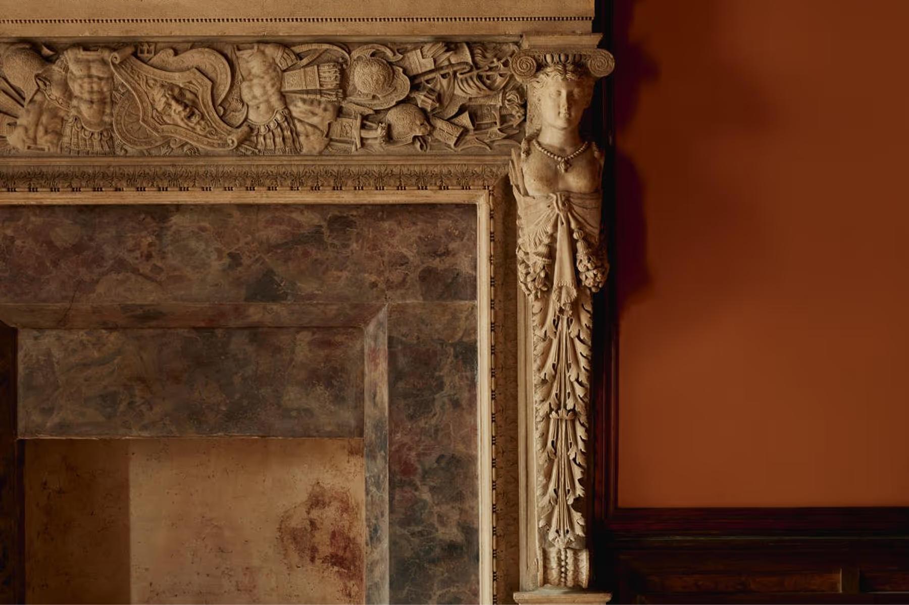 A close detail of an ornate fireplace mantel with carved stone decoration in cream and terracotta