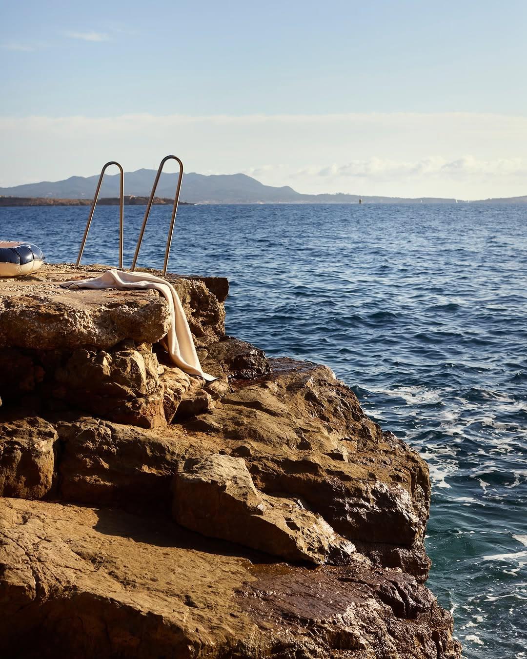 A steel sea ladder descends the rocky shoreline toward the open Mediterranean