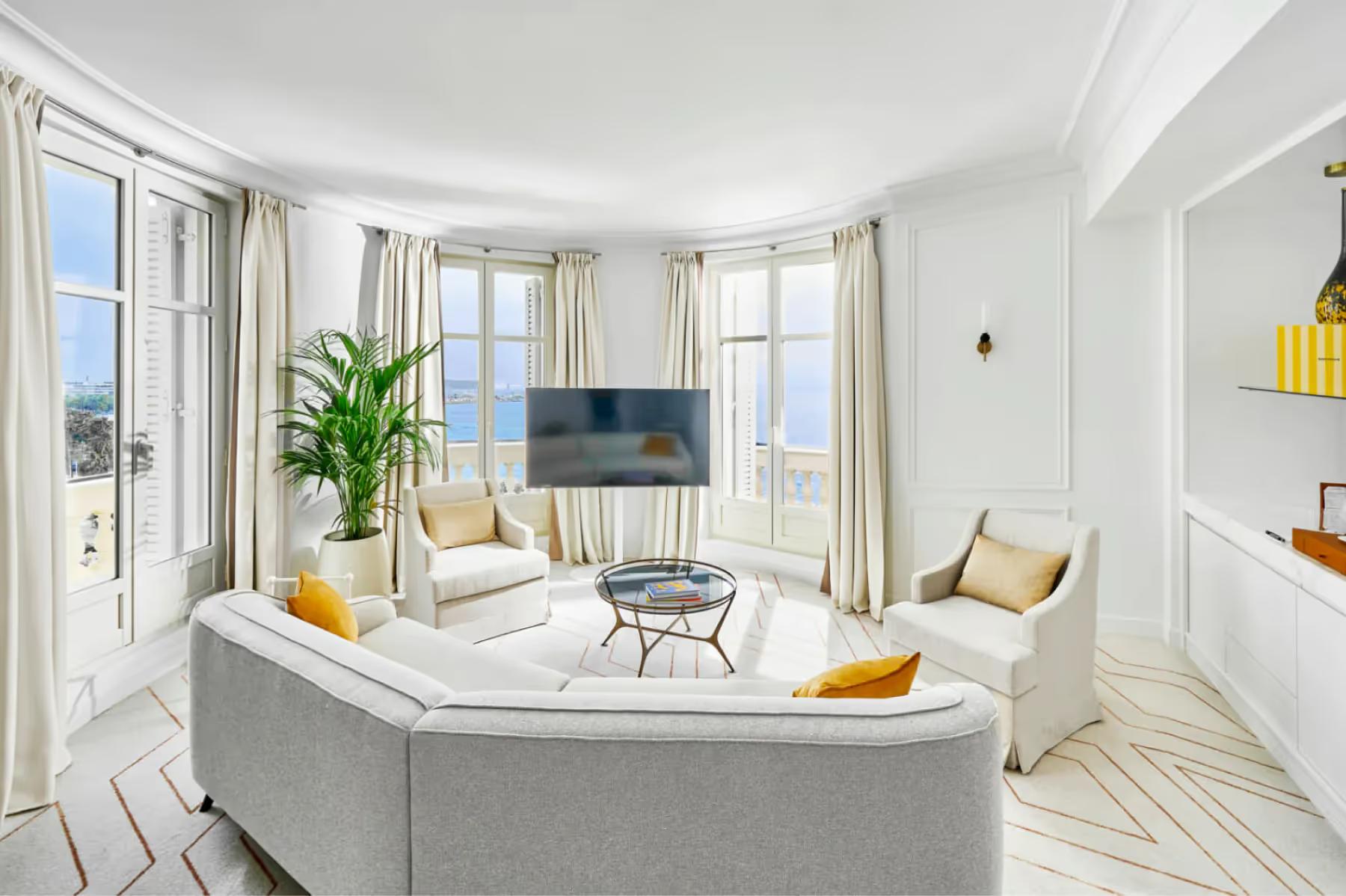Suite living area with light gray sofa, multiple windows, and furnishings in cream and yellow tones