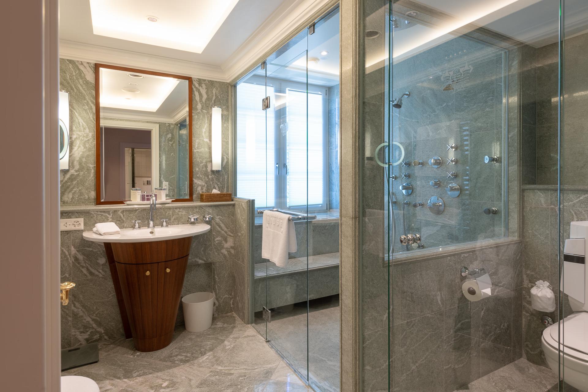 Suvretta House: a spa bathroom with wooden vanity, glass shower enclosure, and large windows with alpine light