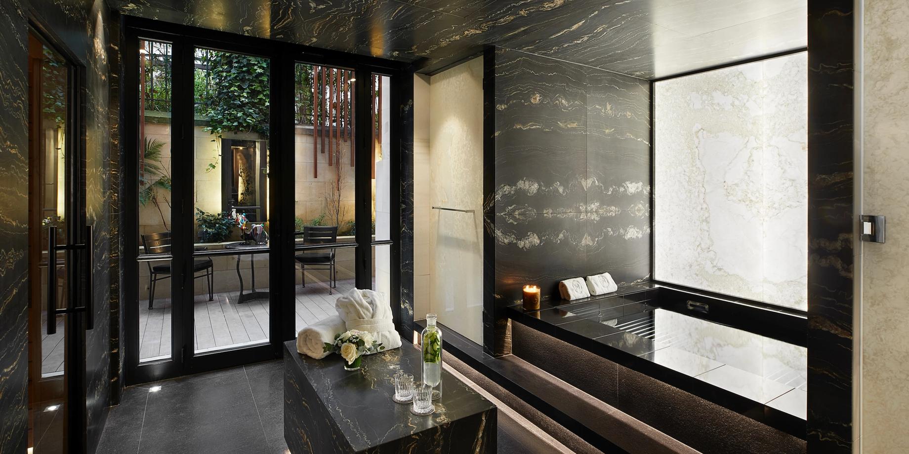 A dark spa interior with glass doors opening to a garden, pale marble walls, and modern furnishings