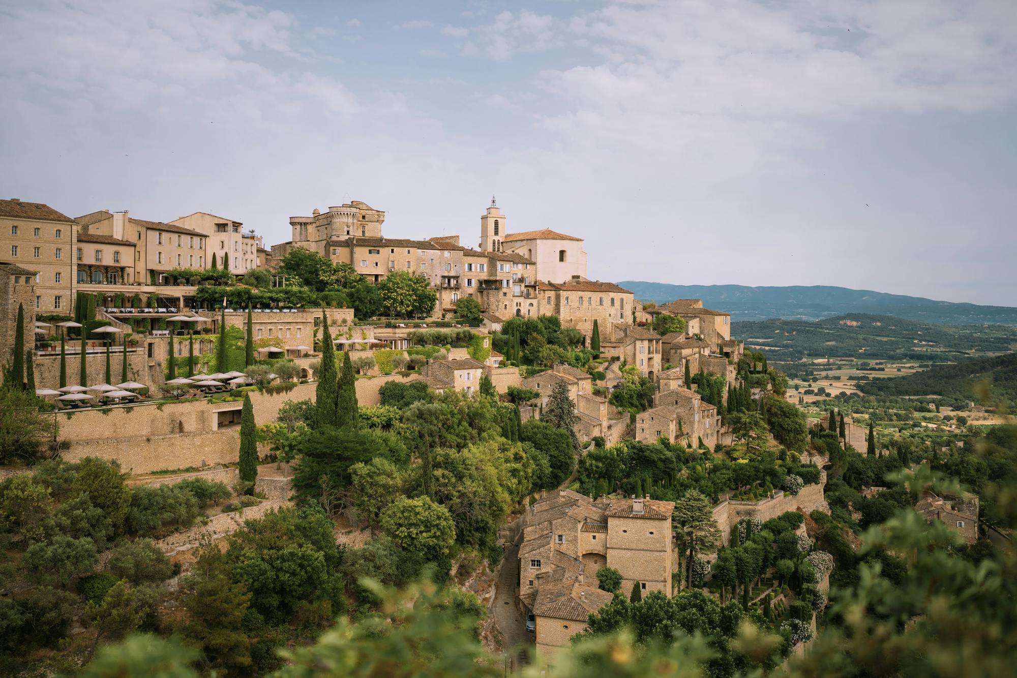 Airelles Gordes, La Bastide: village on a hillside with stone buildings and cypress trees