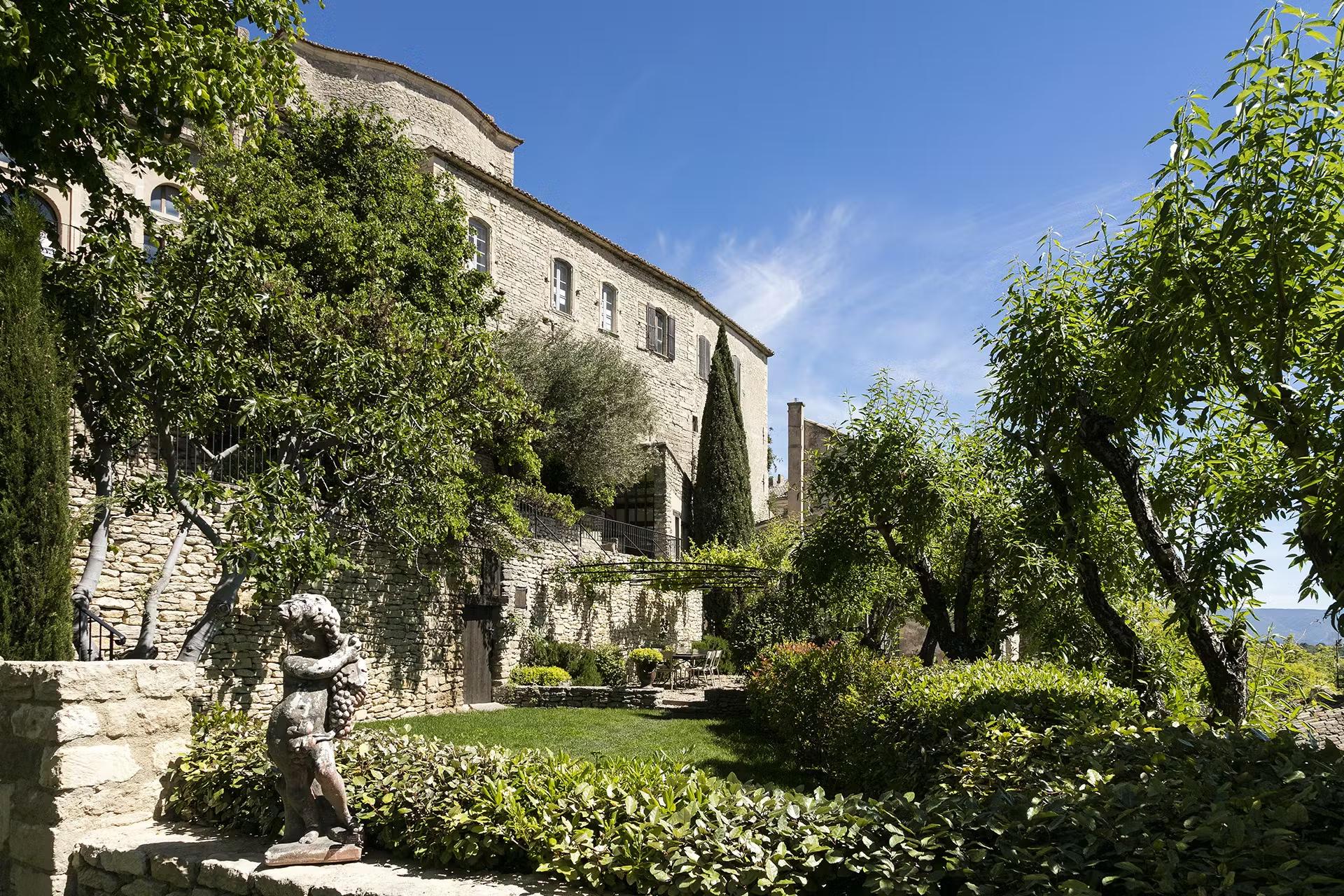 Airelles Gordes, La Bastide: hotel exterior with stone walls, cypress trees, and manicured hedges in afternoon sun