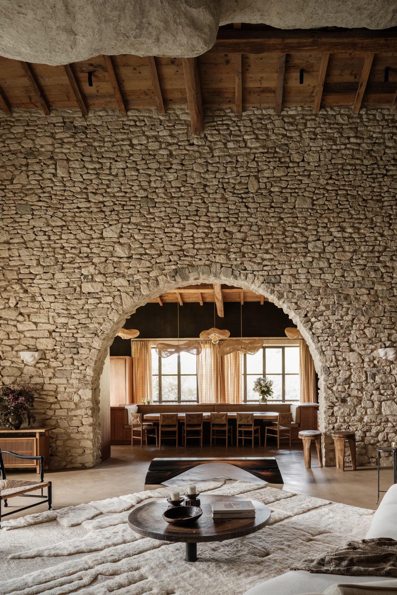 A wide arch in an old stone wall, a dining table under wooden beams beyond