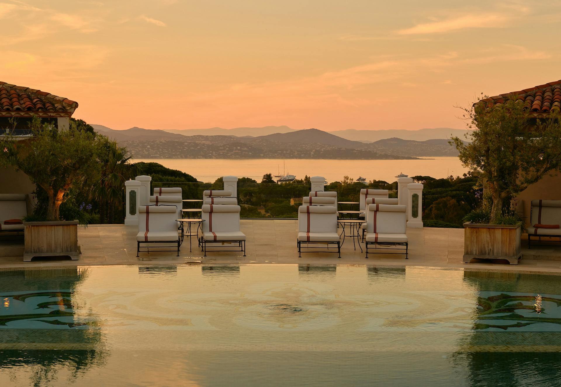 Château de La Messardière: sunset reflection on still pool water with lounge chairs arranged at twilight