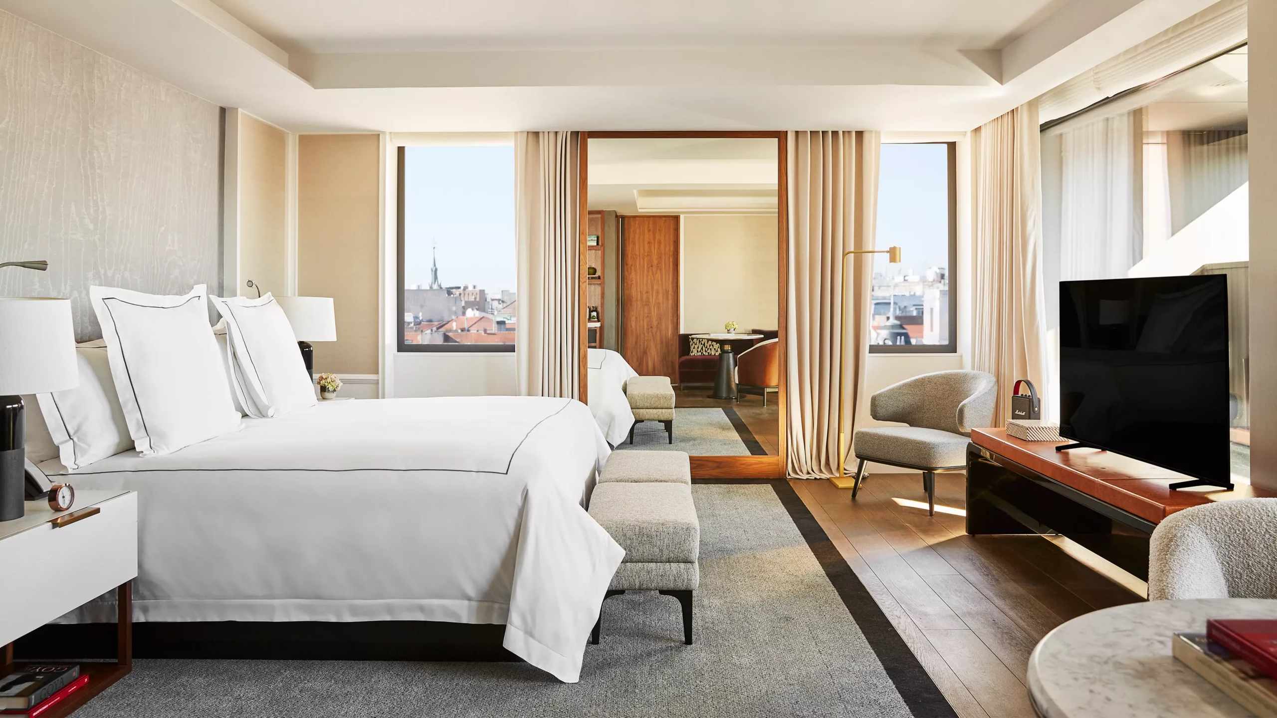 Rosewood Villa Magna: a guest room with white bedding, floor-to-ceiling windows with city views, and warm wood accents