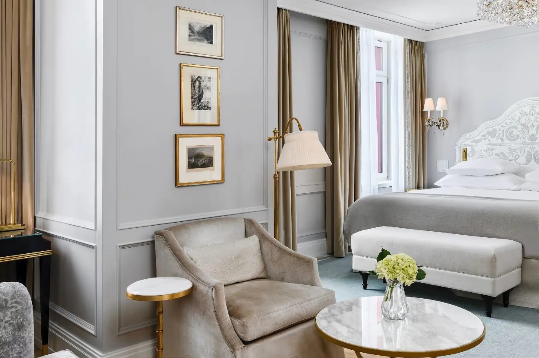 Badrutt’s Palace Hotel: elegant suite with upholstered armchairs, sofa, framed artwork, and bedside flowers