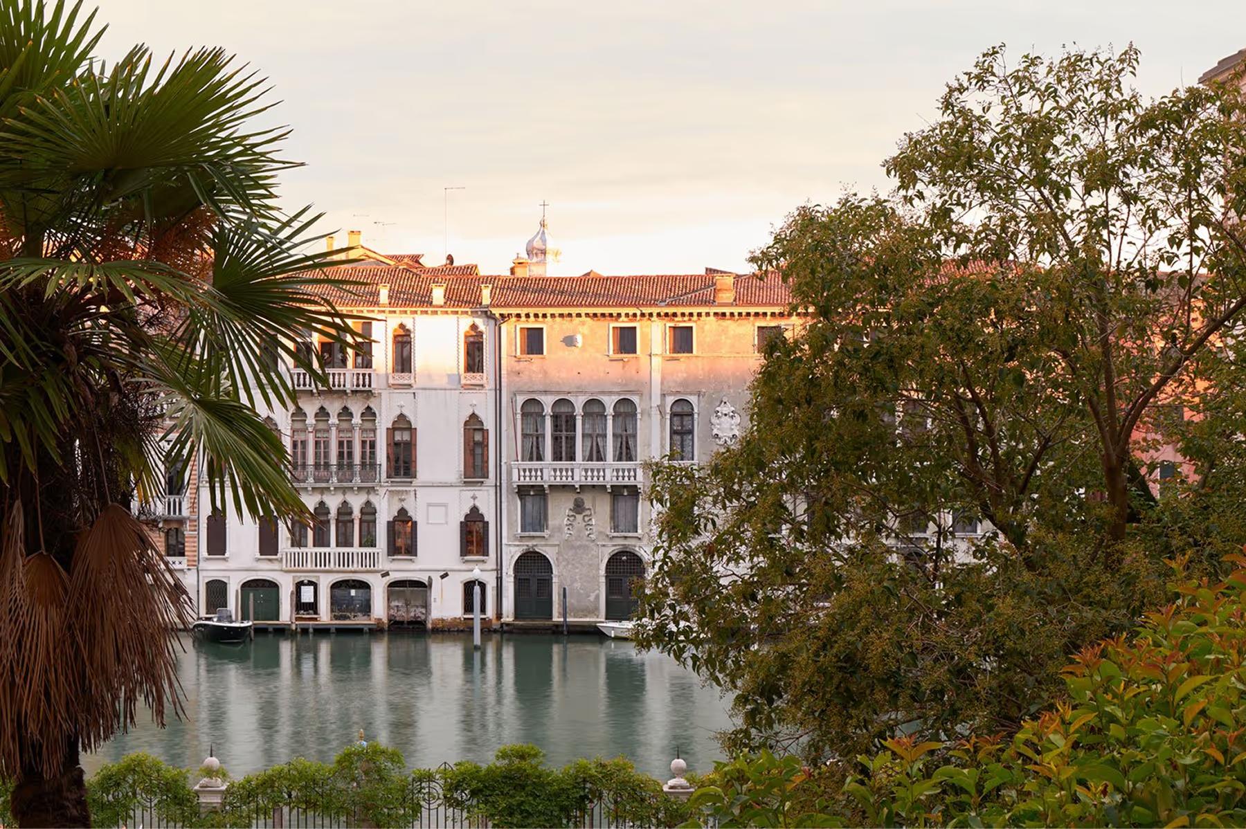 Aman Venice: the palazzo exterior with palm trees and Grand Canal waterfront in evening light