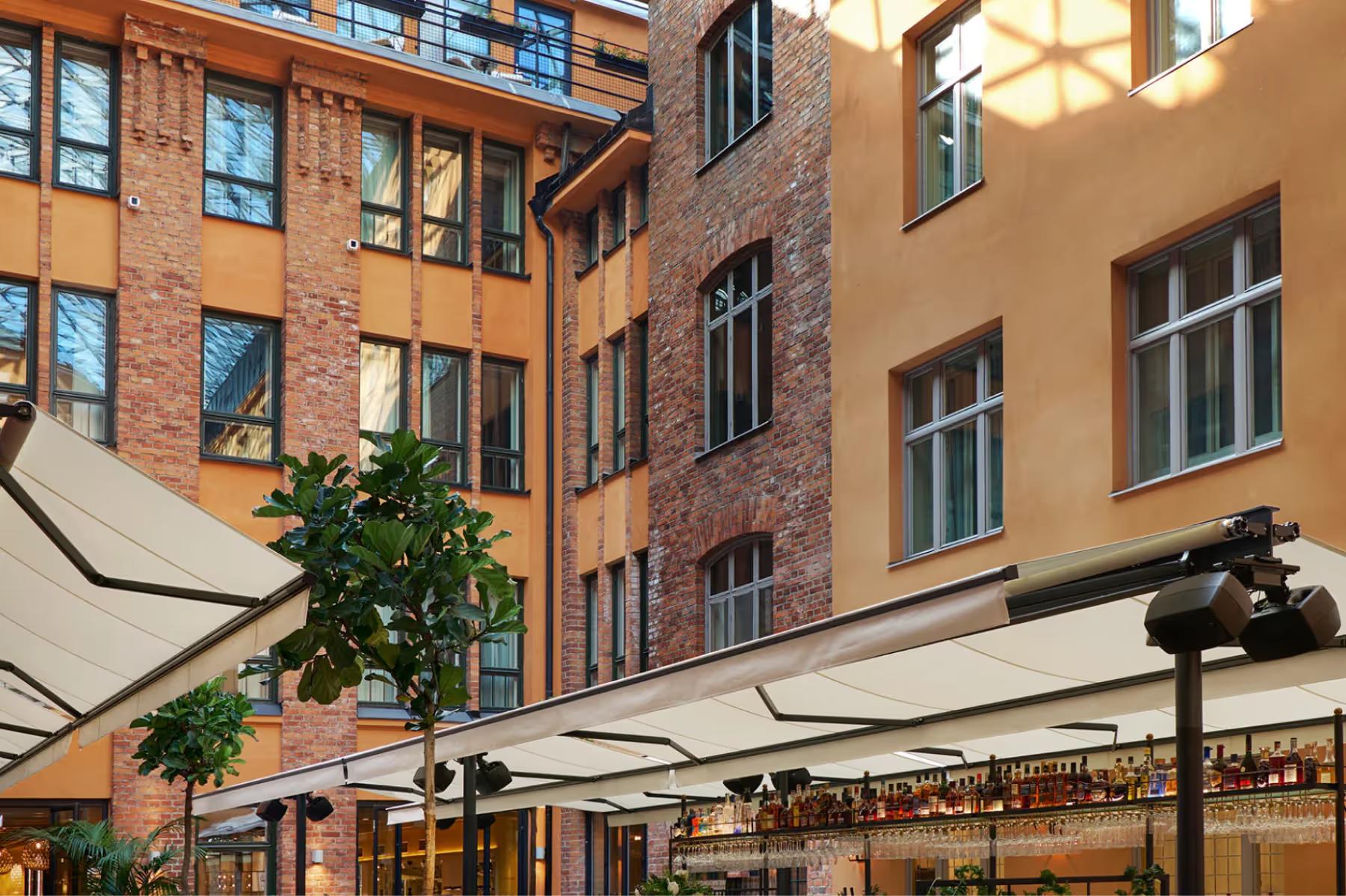 Villa Dagmar: colorful brick courtyard building with outdoor cafe seating and shade structures