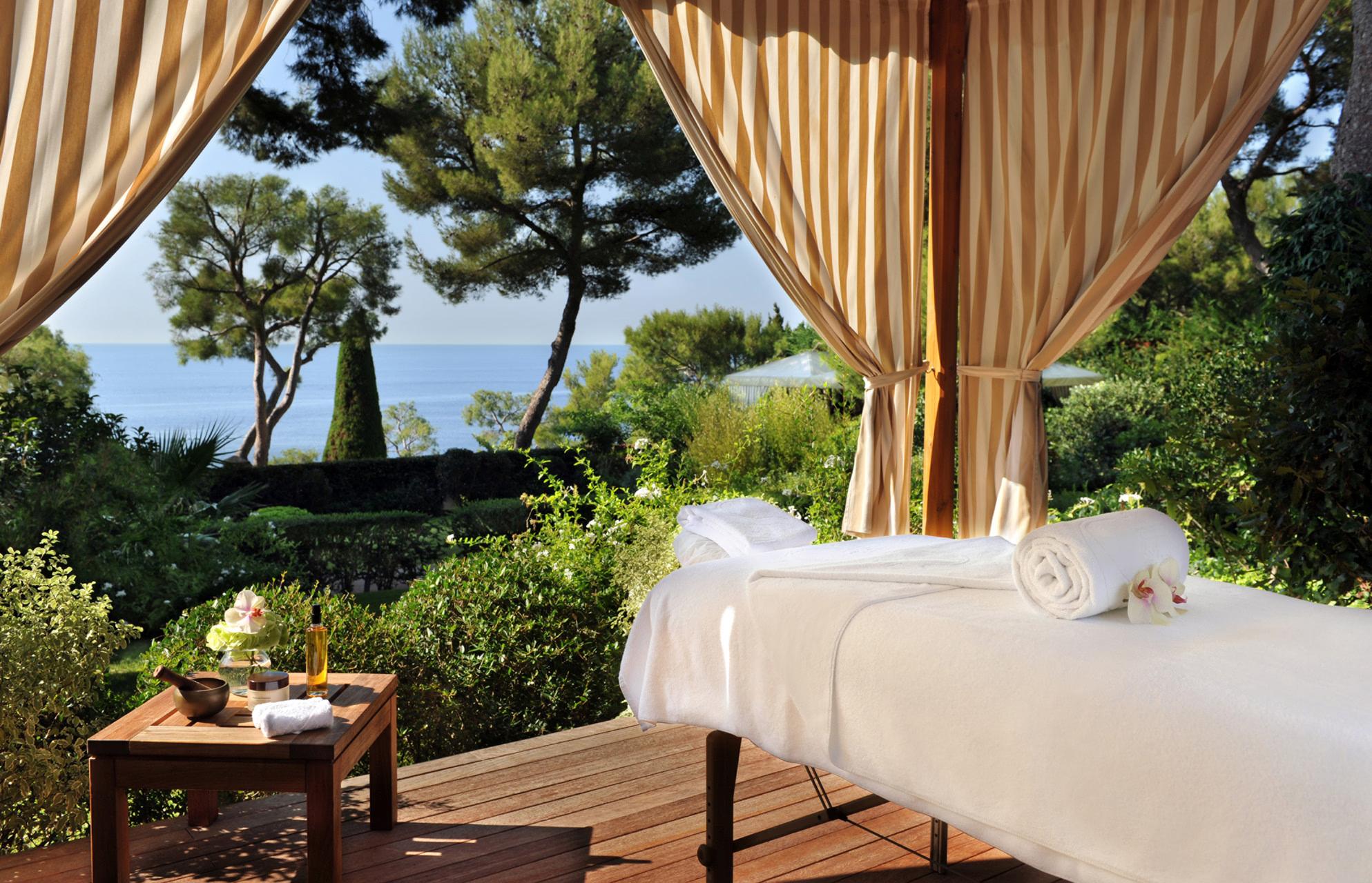 Spa pavilion with massage bed beneath draped curtains and garden view