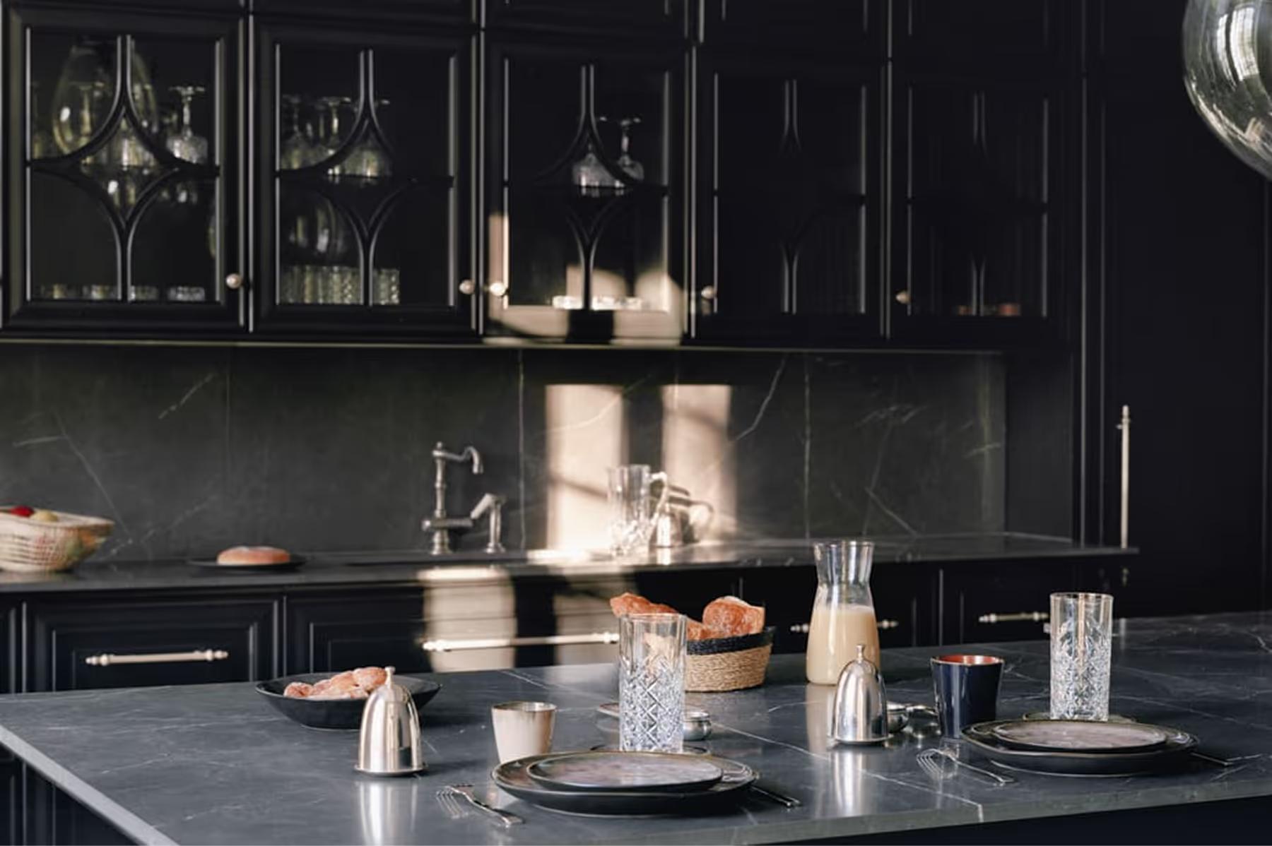 Minimalist black kitchen with dark cabinetry, brass fixtures, and white stone countertop