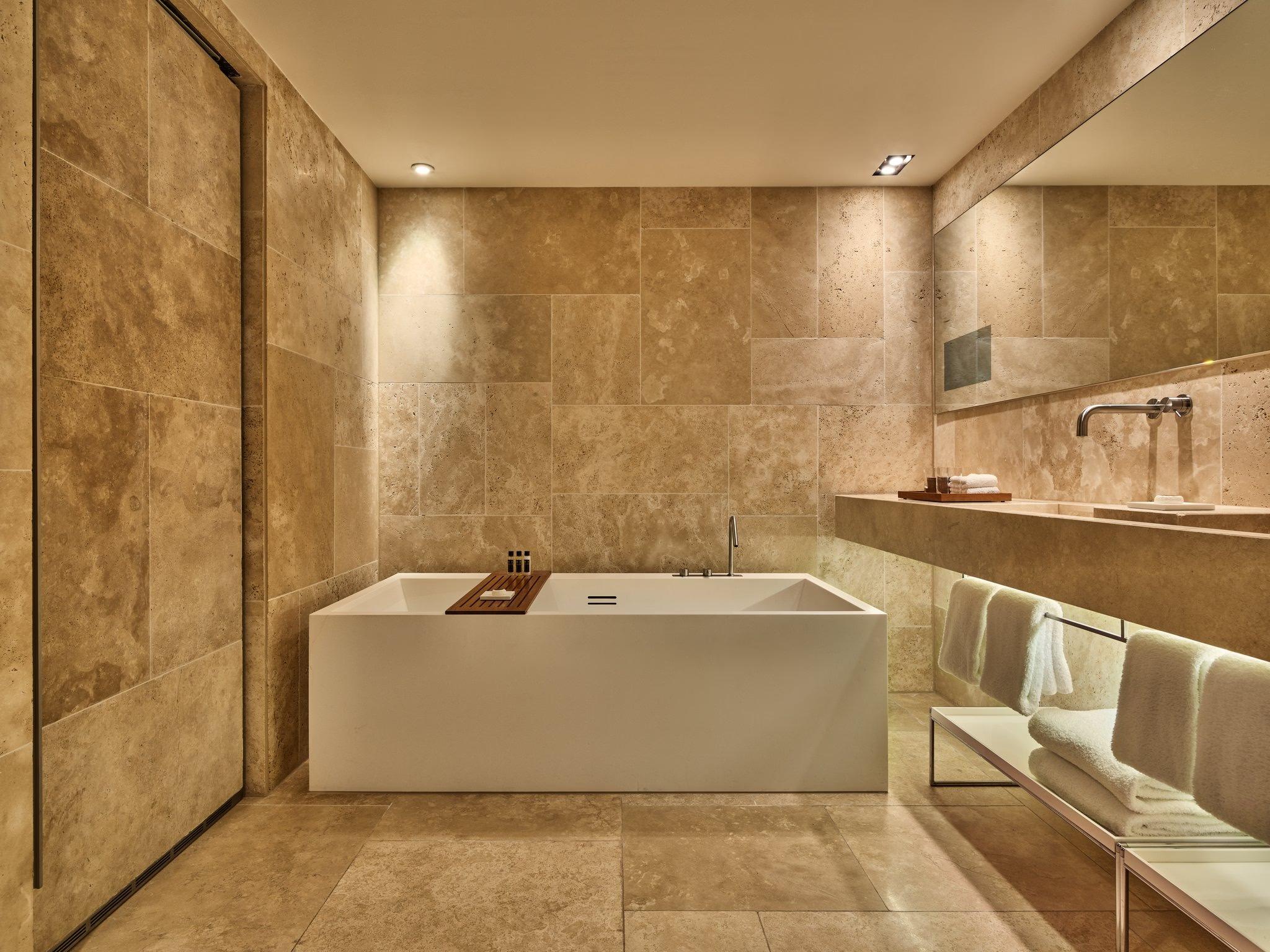 Mandarin Oriental Conservatorium, Amsterdam: stone-clad bathroom with a freestanding white bathtub, a long stone vanity, and folded white towels