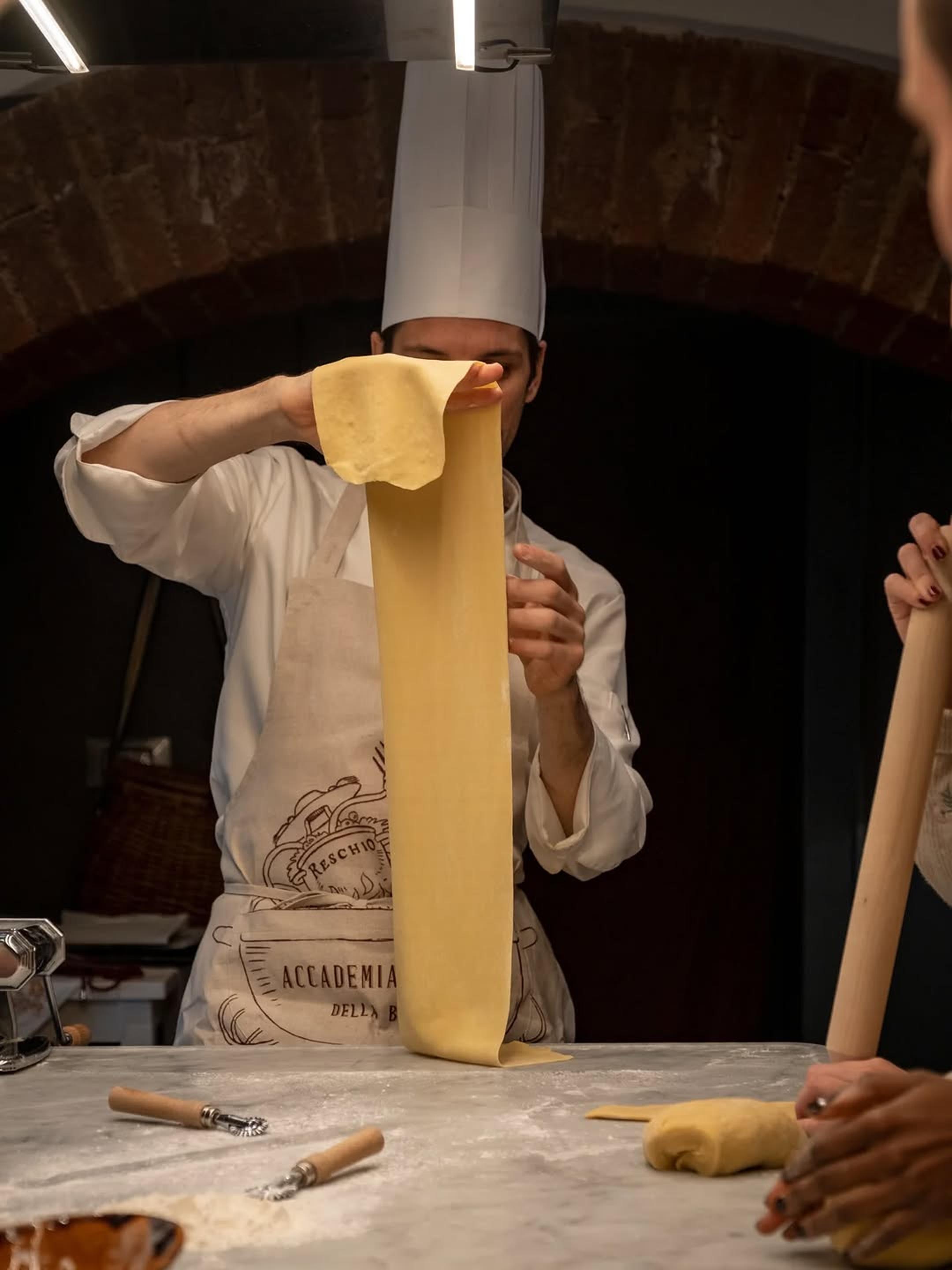 A chef stretching pasta dough by hand beneath the stone arches of the kitchen