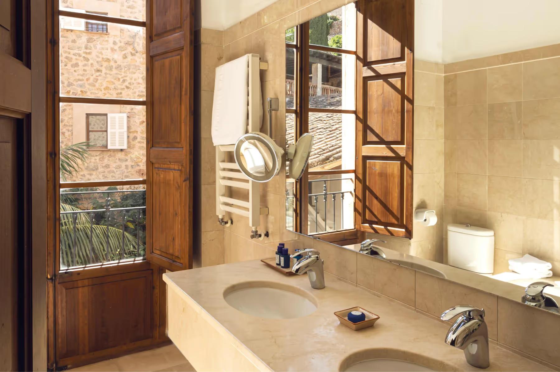 La Residencia: bathroom with double sink vanity, wooden doors, framed mirrors, and view to village landscape