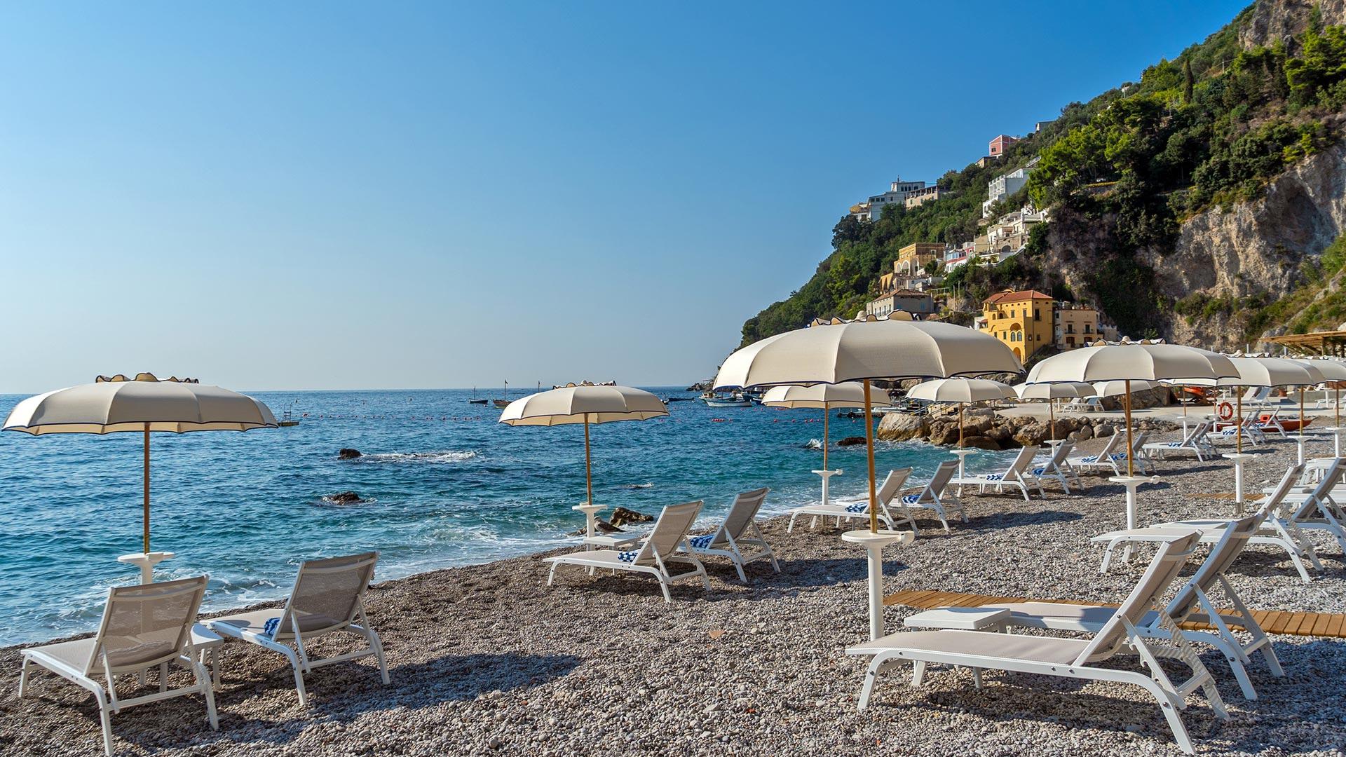Borgo Santandrea: beach with loungers and umbrellas beside rocky promontory and clear blue water