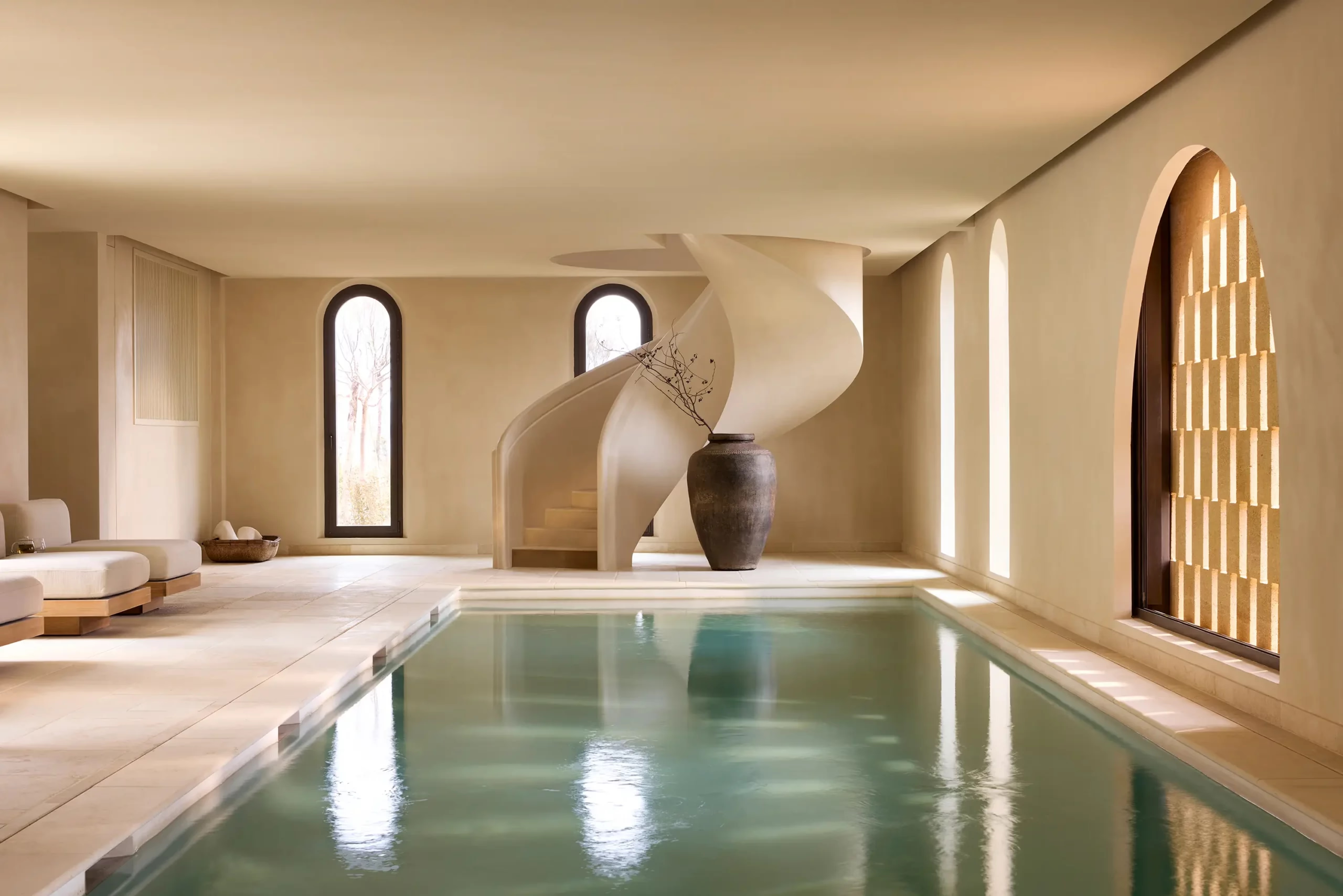 A sculptural spiral stair curves past a clay urn beside the indoor spa pool