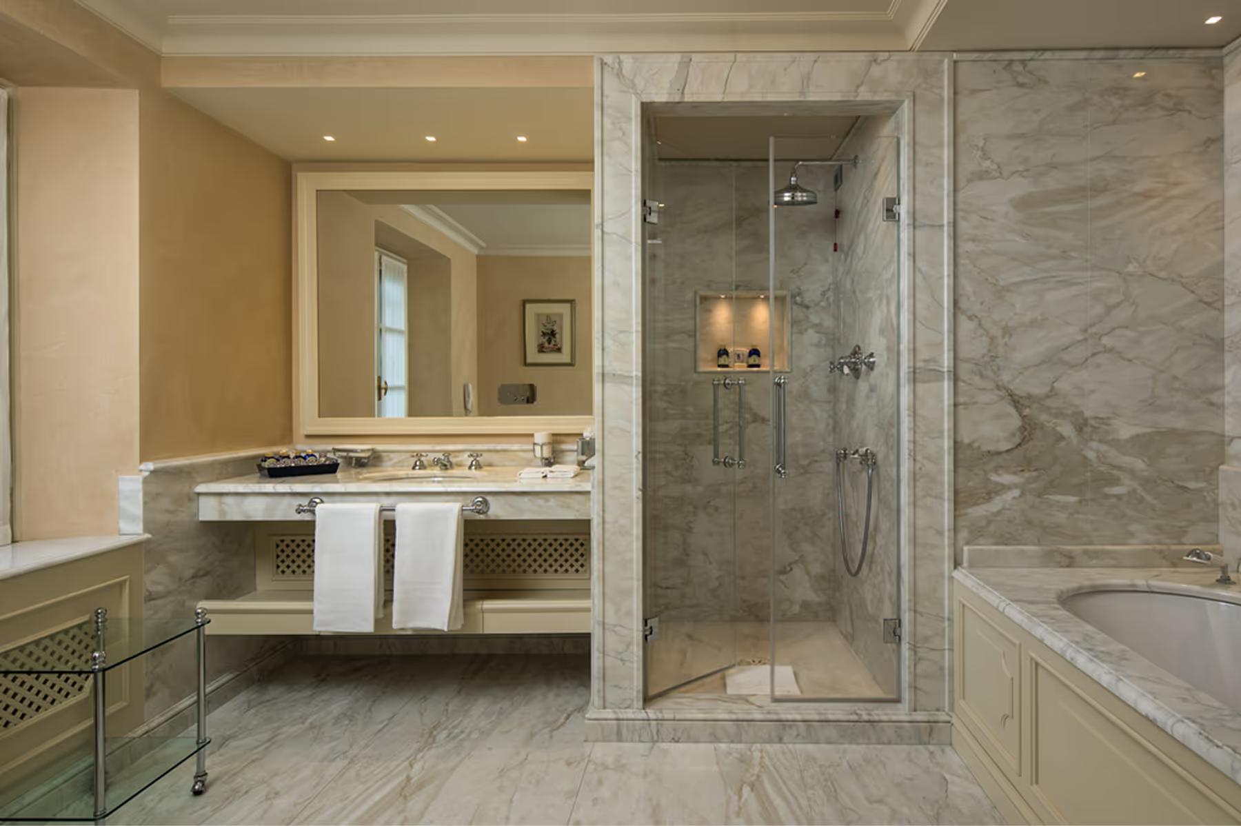 Marble bathroom with dual sinks, frameless glass shower enclosure, and polished stone surfaces