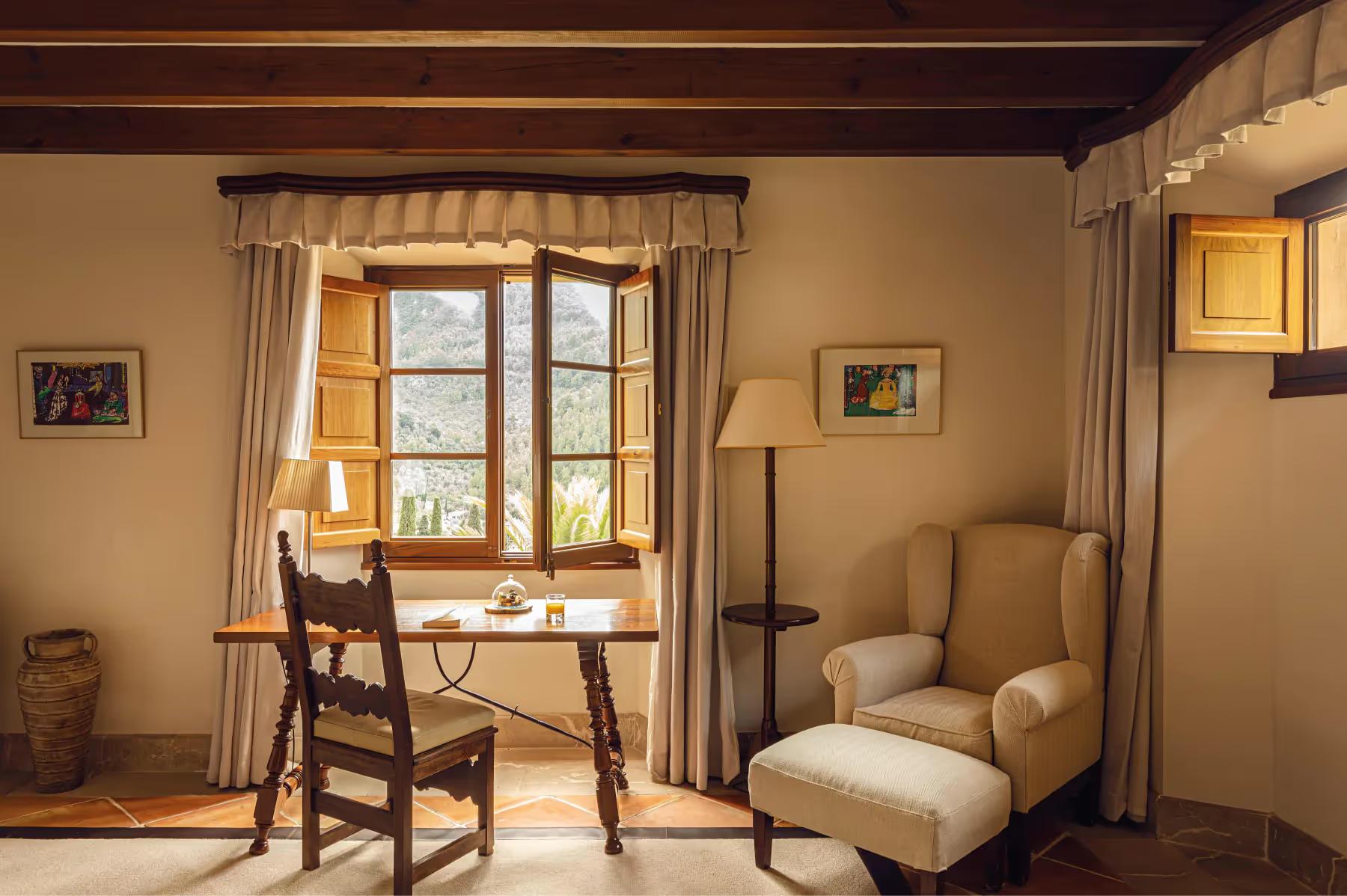 Suite with beamed wooden ceiling, window desk, upholstered chair, and warm cream walls