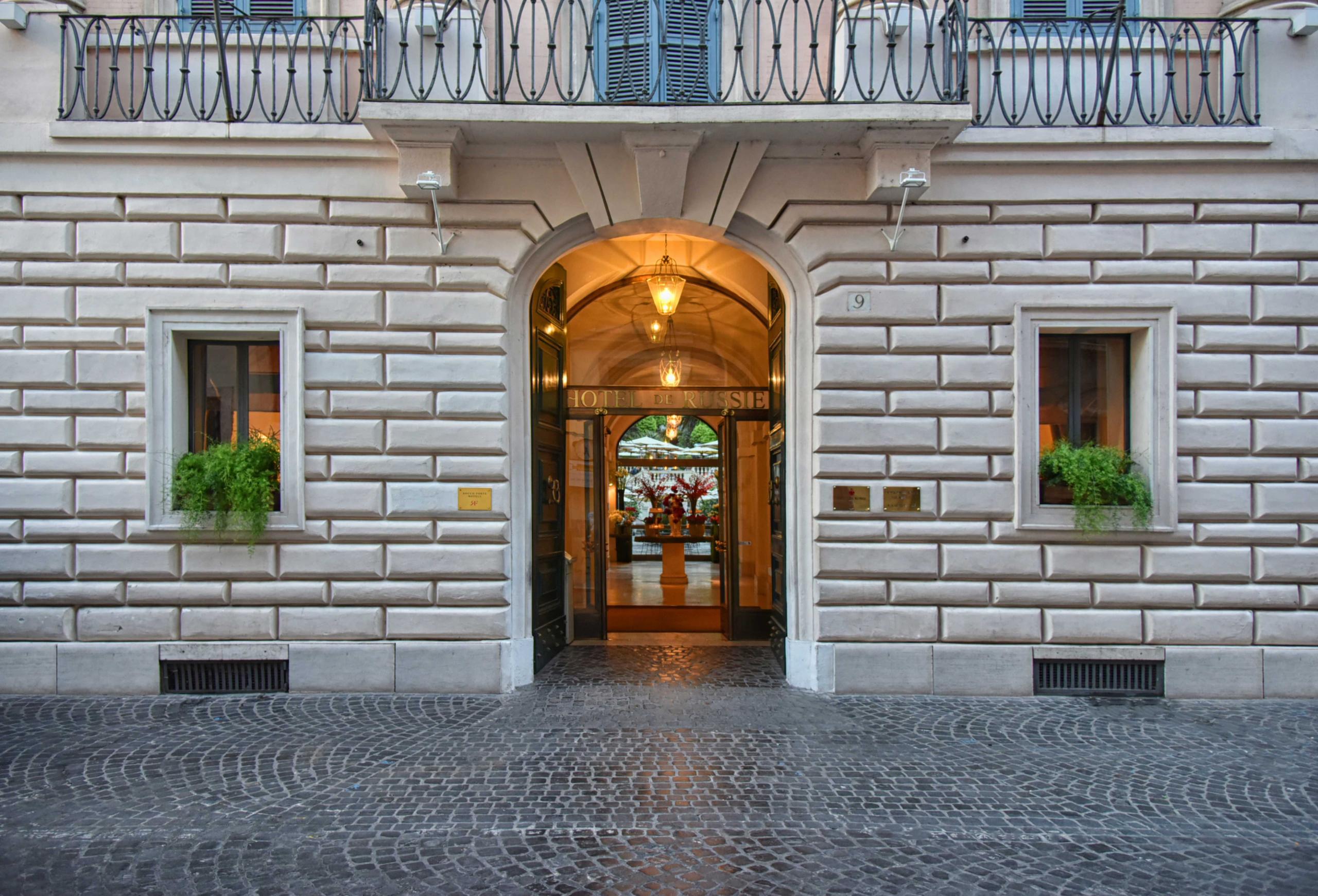 Hotel de Russie: arched palazzo entrance with warm lighting and potted plants at street level