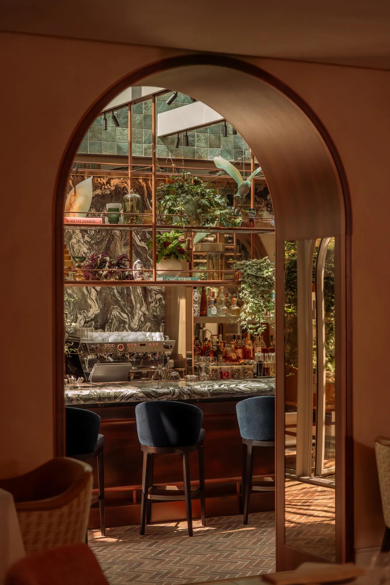 Rosewood Amsterdam: an arched doorway at Eeuwen that opens onto the bar and its hanging plants