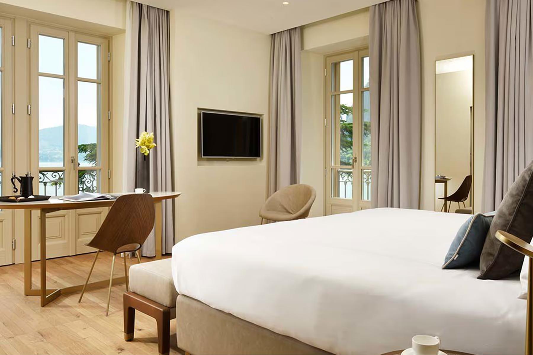 A spacious bedroom with light wood floors, large windows, and a desk