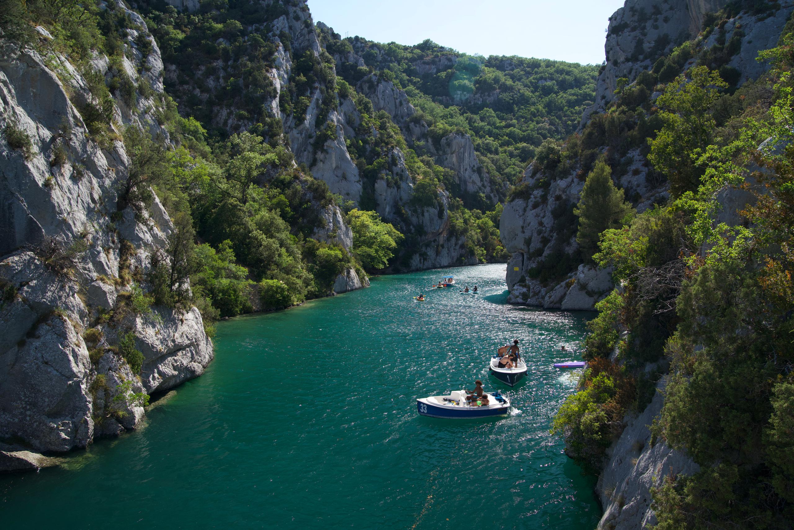Small boats on the turquoise water of the lower Verdon gorge, between limestone cliffs