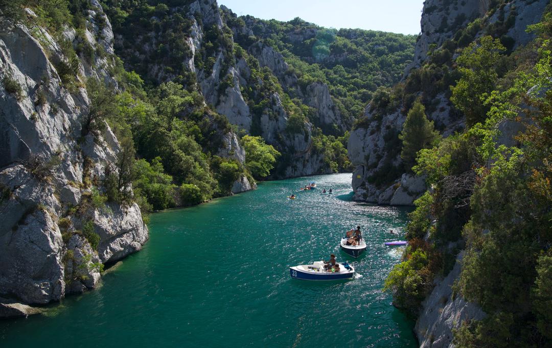 Small boats on the turquoise water of the lower Verdon gorge, between limestone cliffs