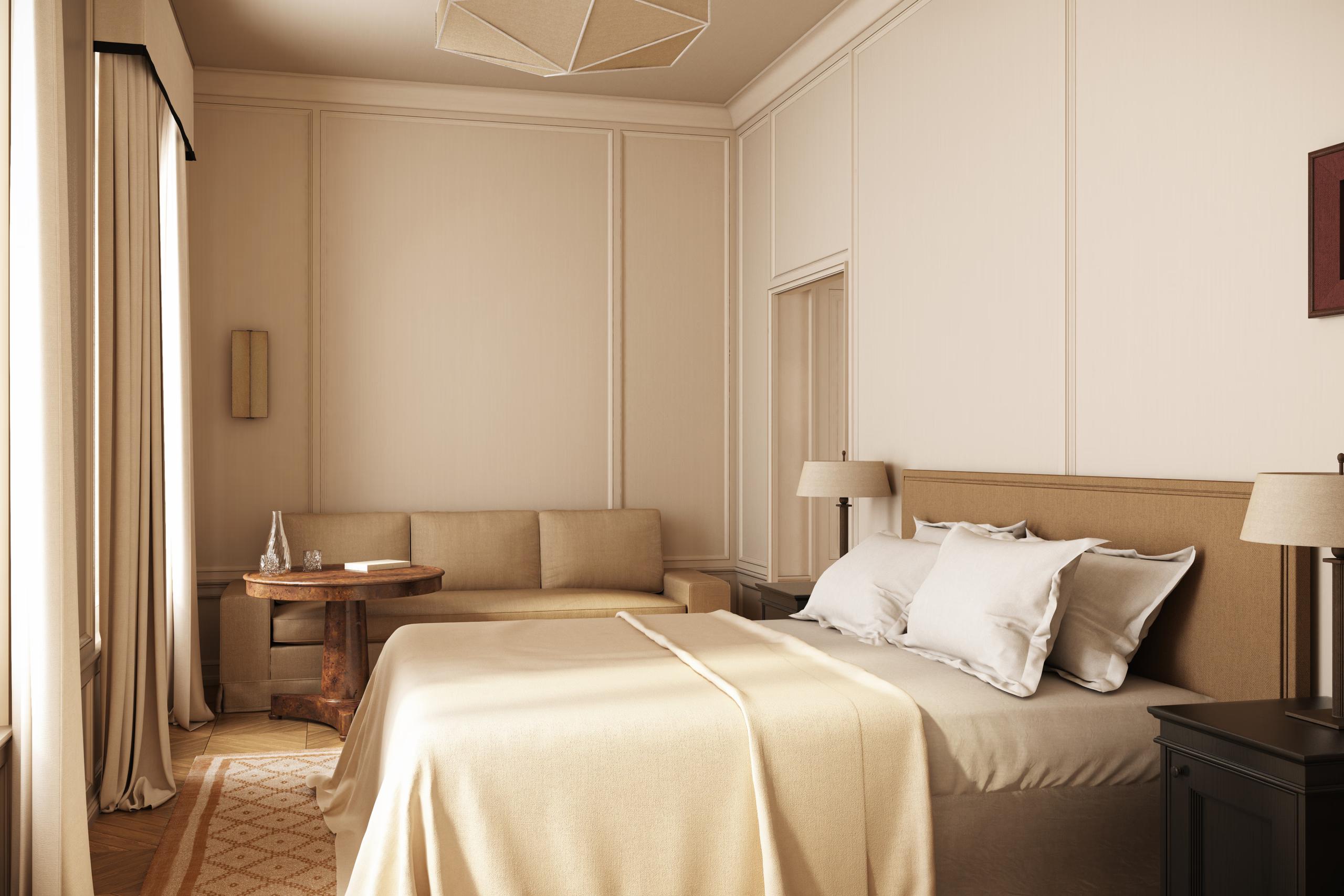 A bedroom with pale walls, a low bed with tan bedding, and minimal furnishings
