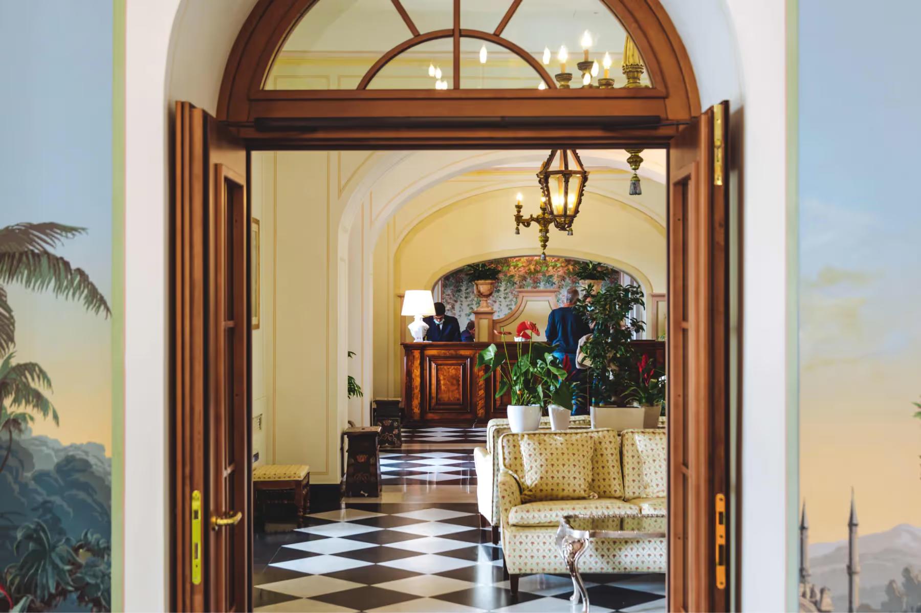 An arched entryway with dark wooden doors opening into a corridor with checkered floor