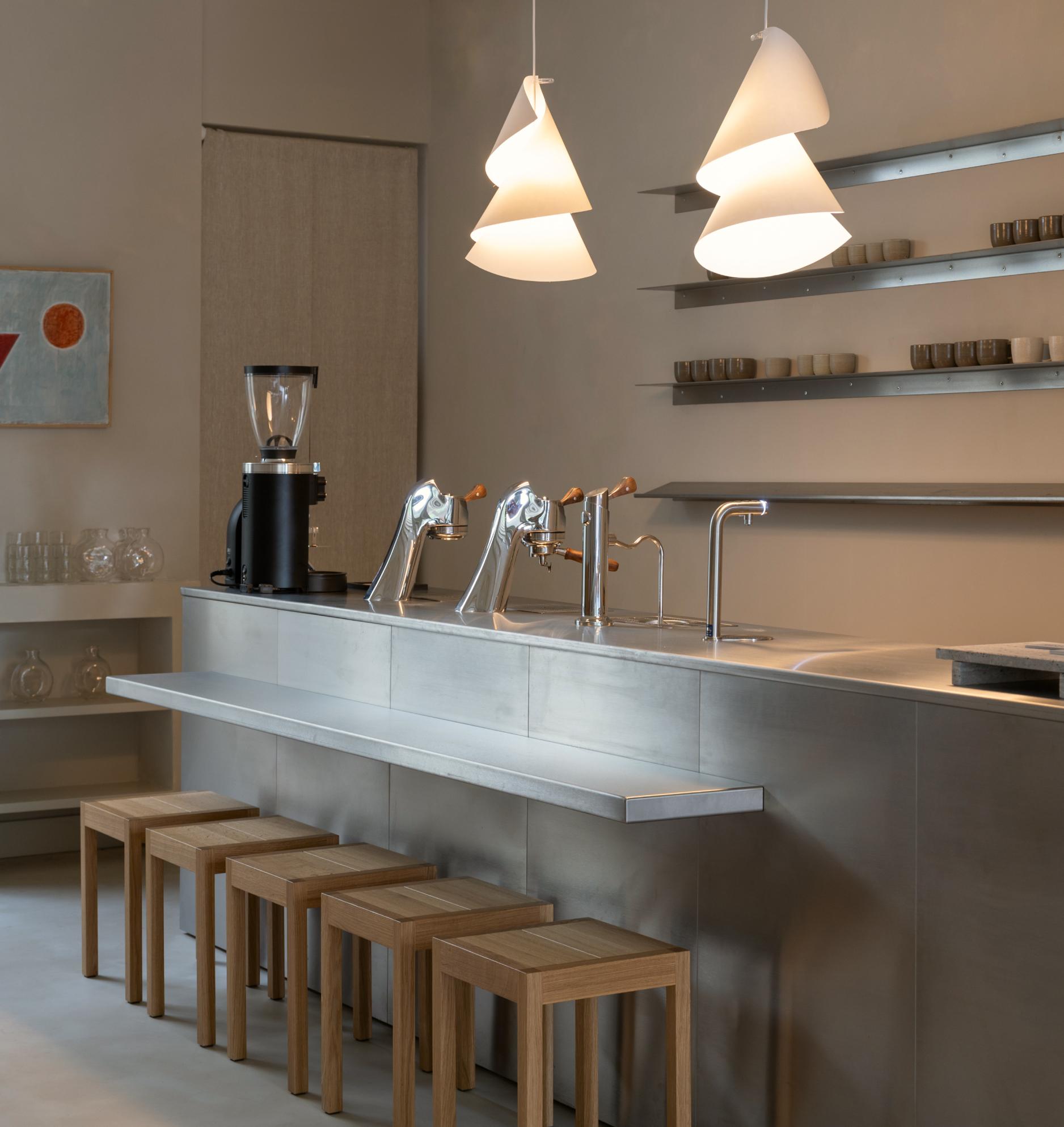 The steel counter at Two Story, espresso machines beneath sculptural pendant lights