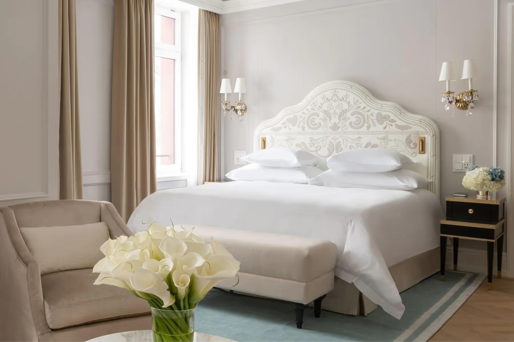 Badrutt’s Palace Hotel: bedroom with ornate white headboard, upholstered armchair, and fresh flowers