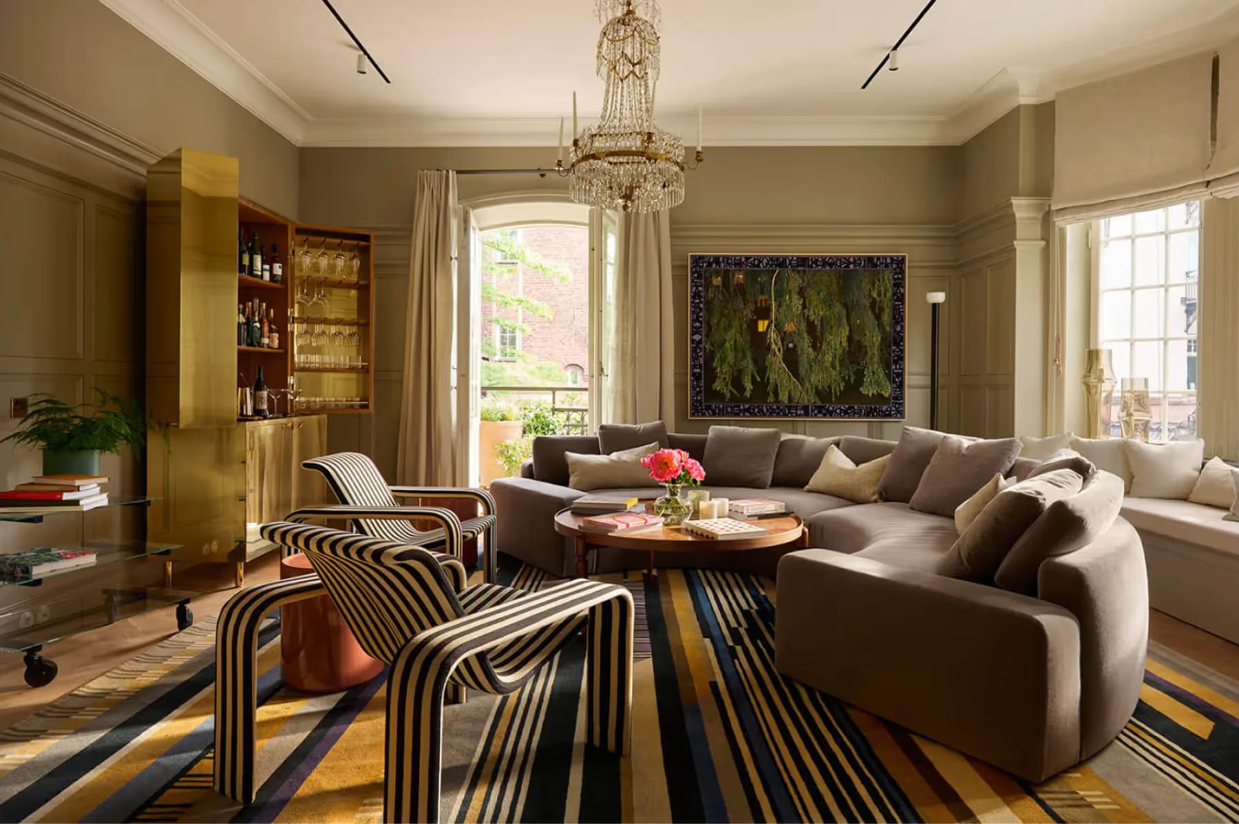 A living room with taupe sofa, striped rug, artwork, and natural light from windows