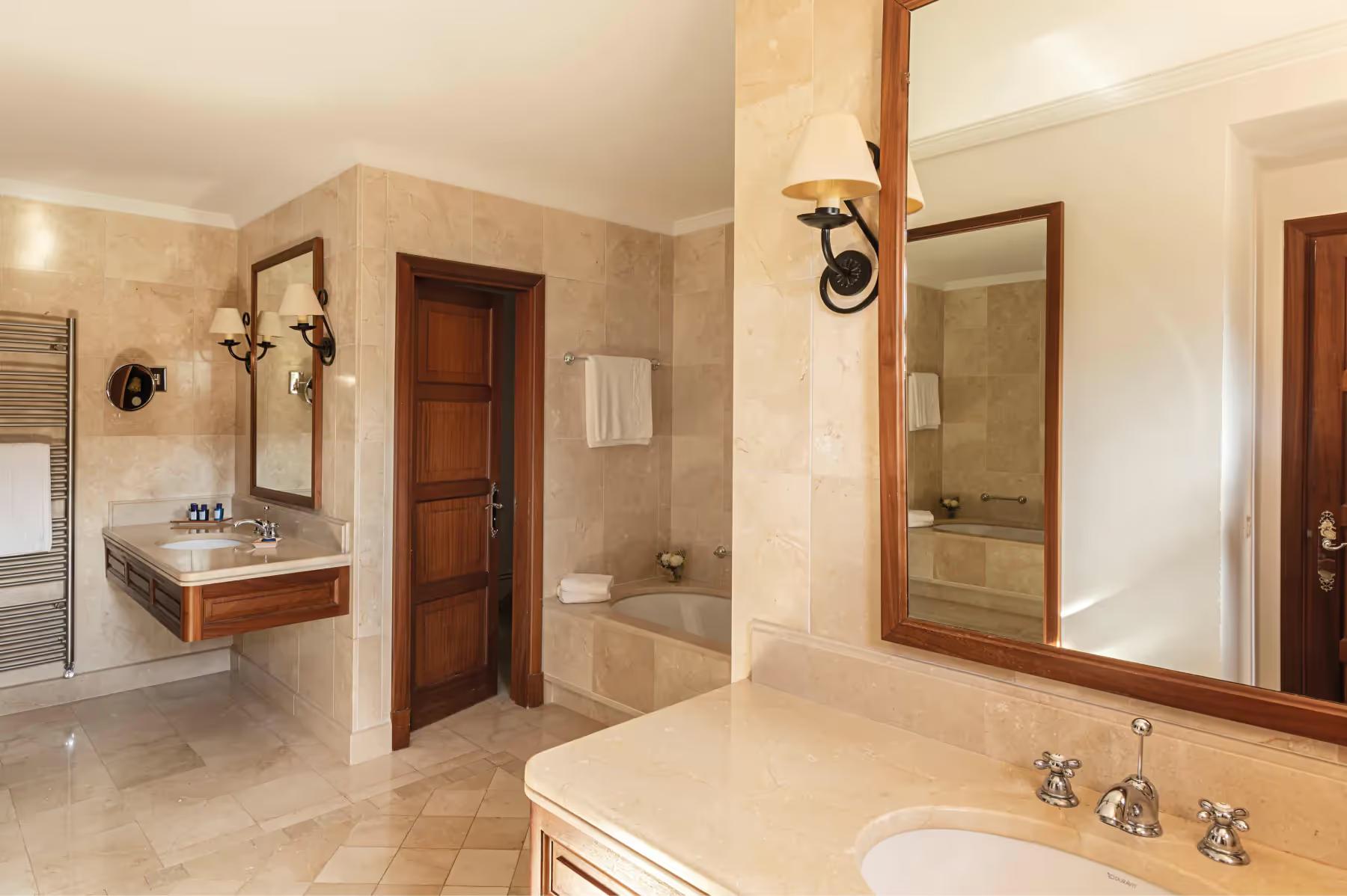 La Residencia: spa-style bathroom with dual vanities, walk-in shower area, and warm natural stone finishes