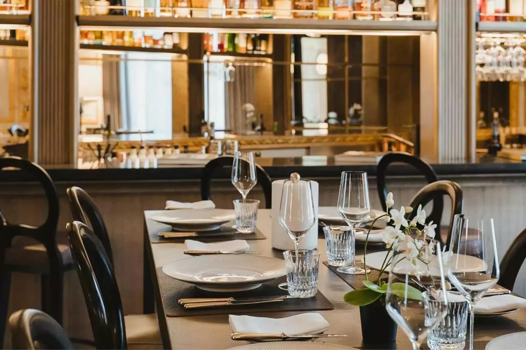 Maison Villeroy: a bar interior with lit shelving behind counter, formal place settings, and glass tabletop