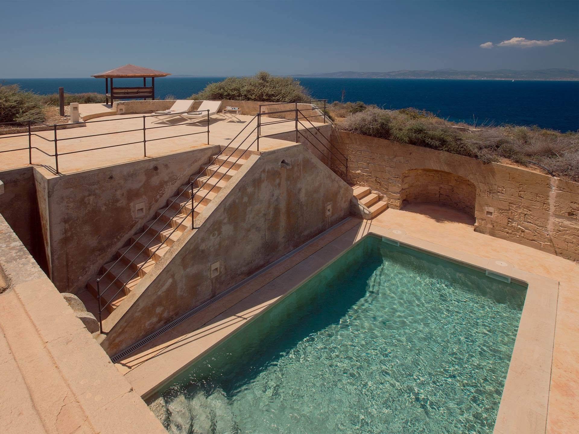 Cap Rocat: a modern saltwater pool in turquoise waters with railing and coastal rock formations