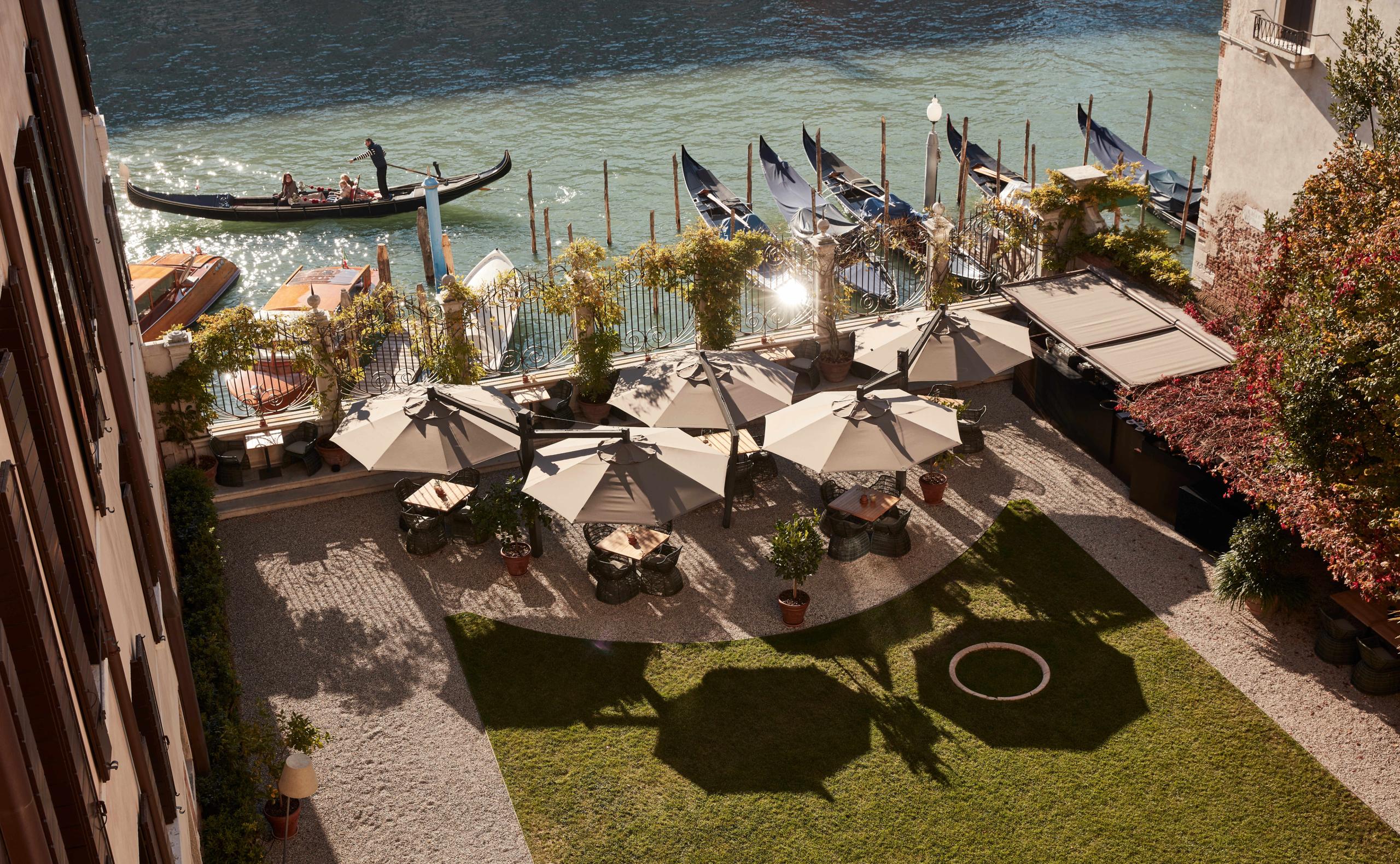 A waterside garden terrace with lounge seating and views of gondolas on the Grand Canal