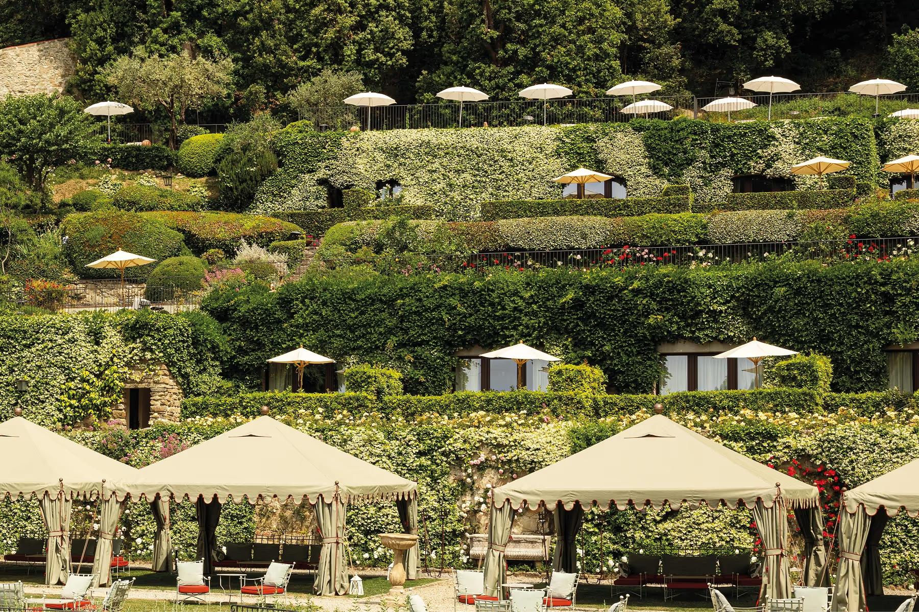 Loungers beneath striped umbrellas in a terraced garden with flowering plants and cypress trees
