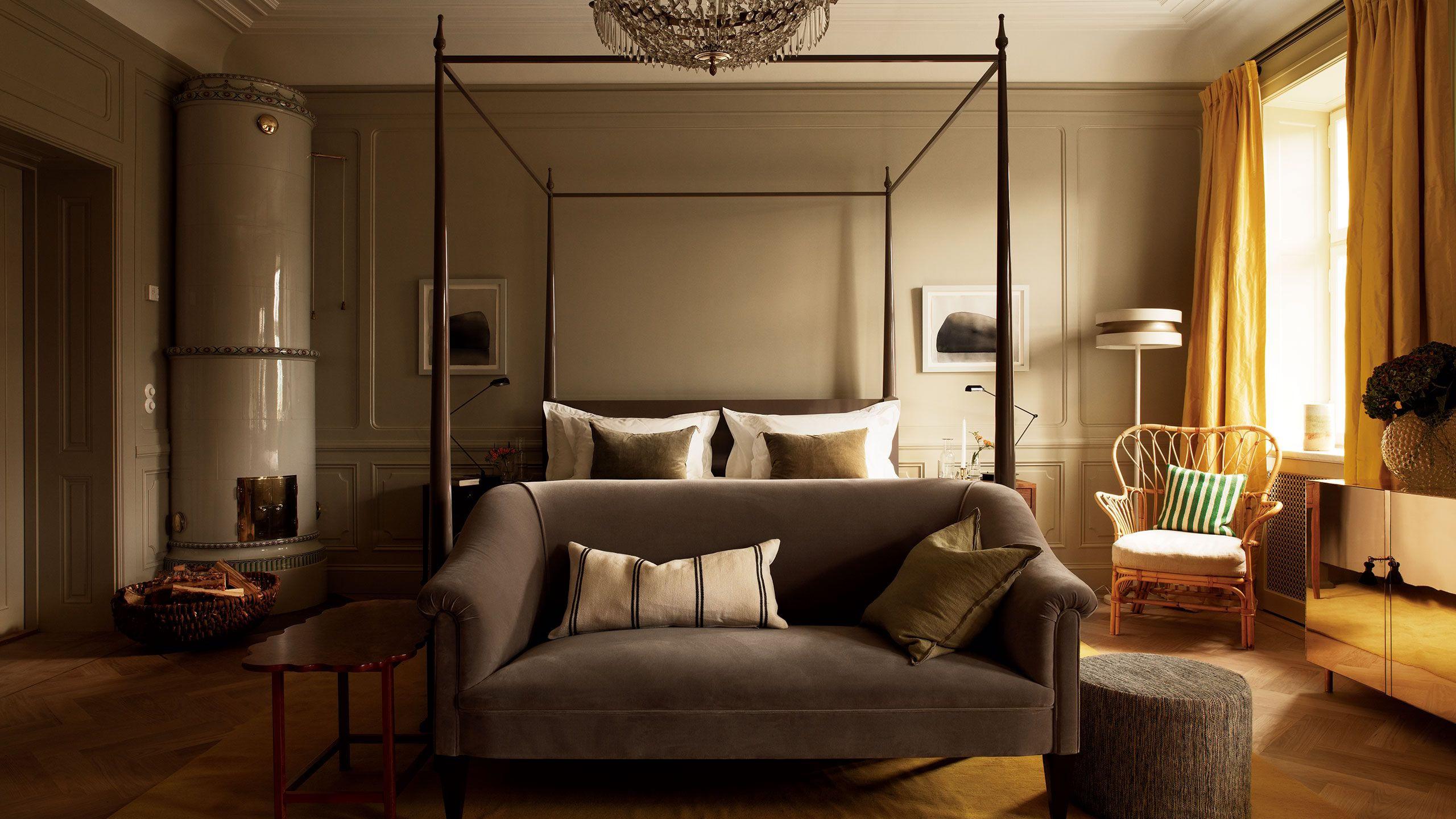 A canopy bed with dark frame and gold cushions in a room with warm neutral walls and tall arched windows