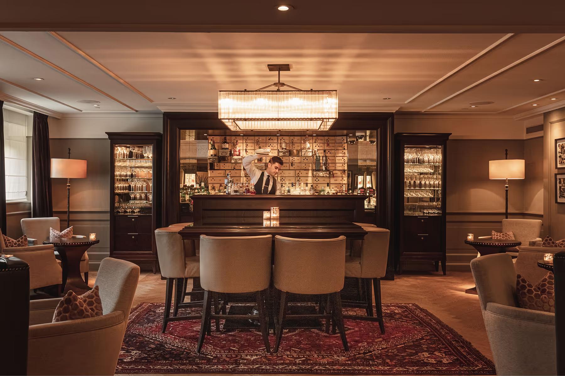 Waldorf Astoria Amsterdam: a bar lounge with dark woodwork, illuminated shelving displaying spirits, and upholstered lounge seating