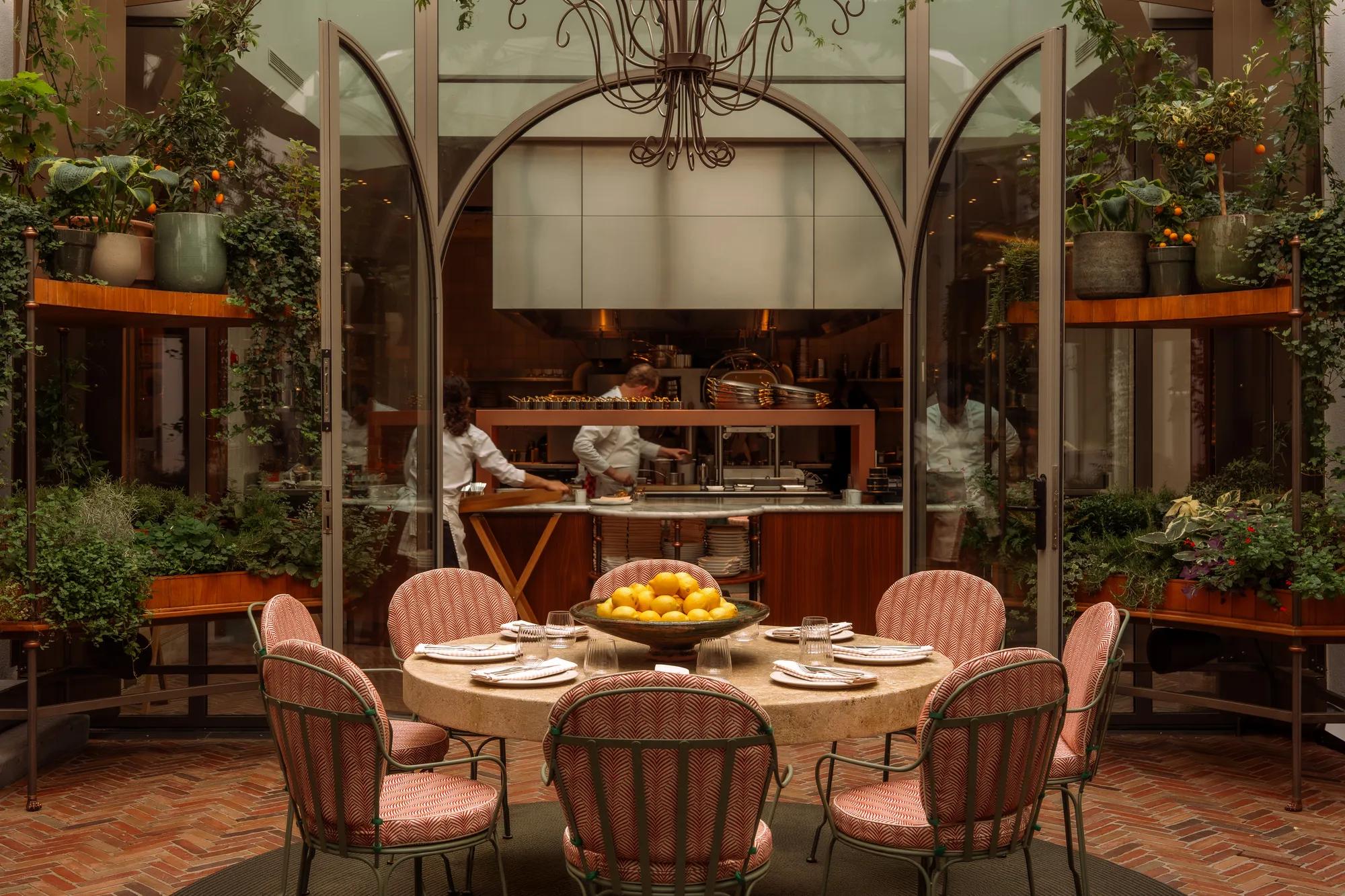 Rosewood Amsterdam: the chef’s table at Eeuwen with pink chairs, plants, and the open kitchen behind