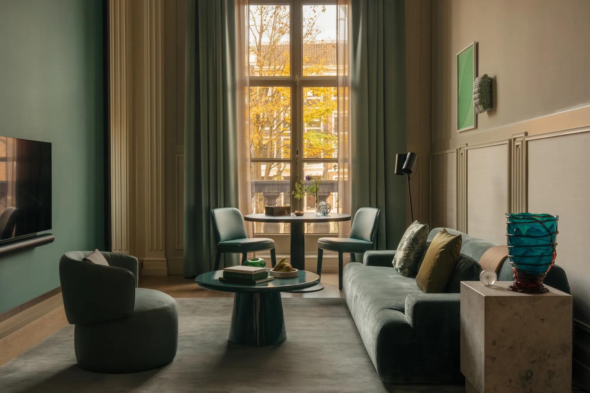 Rosewood Amsterdam: the Canal View Signature Suite living room with a green sofa, armchairs, and a tall window