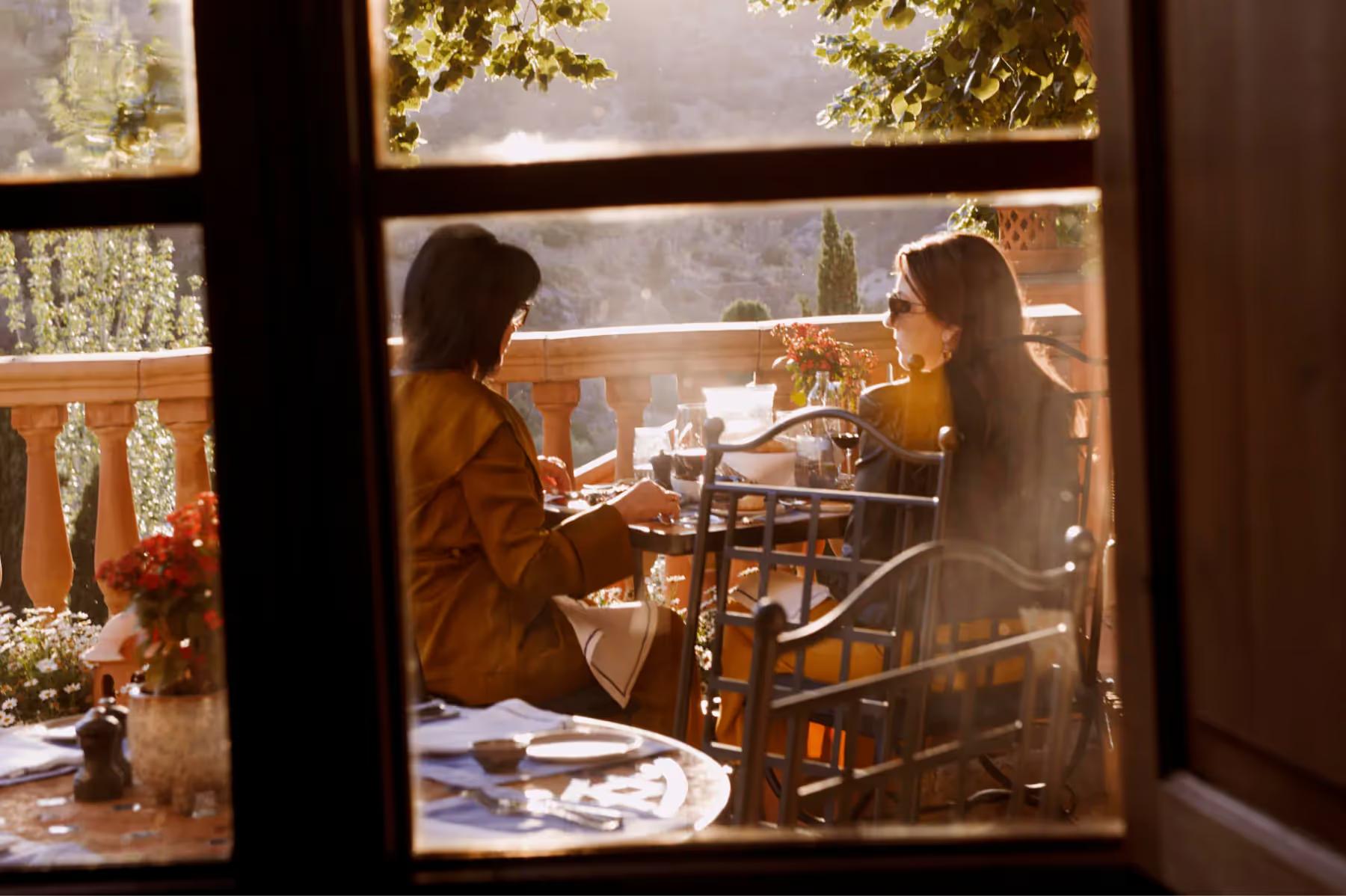 Two diners visible through window frame of restaurant with landscape view beyond
