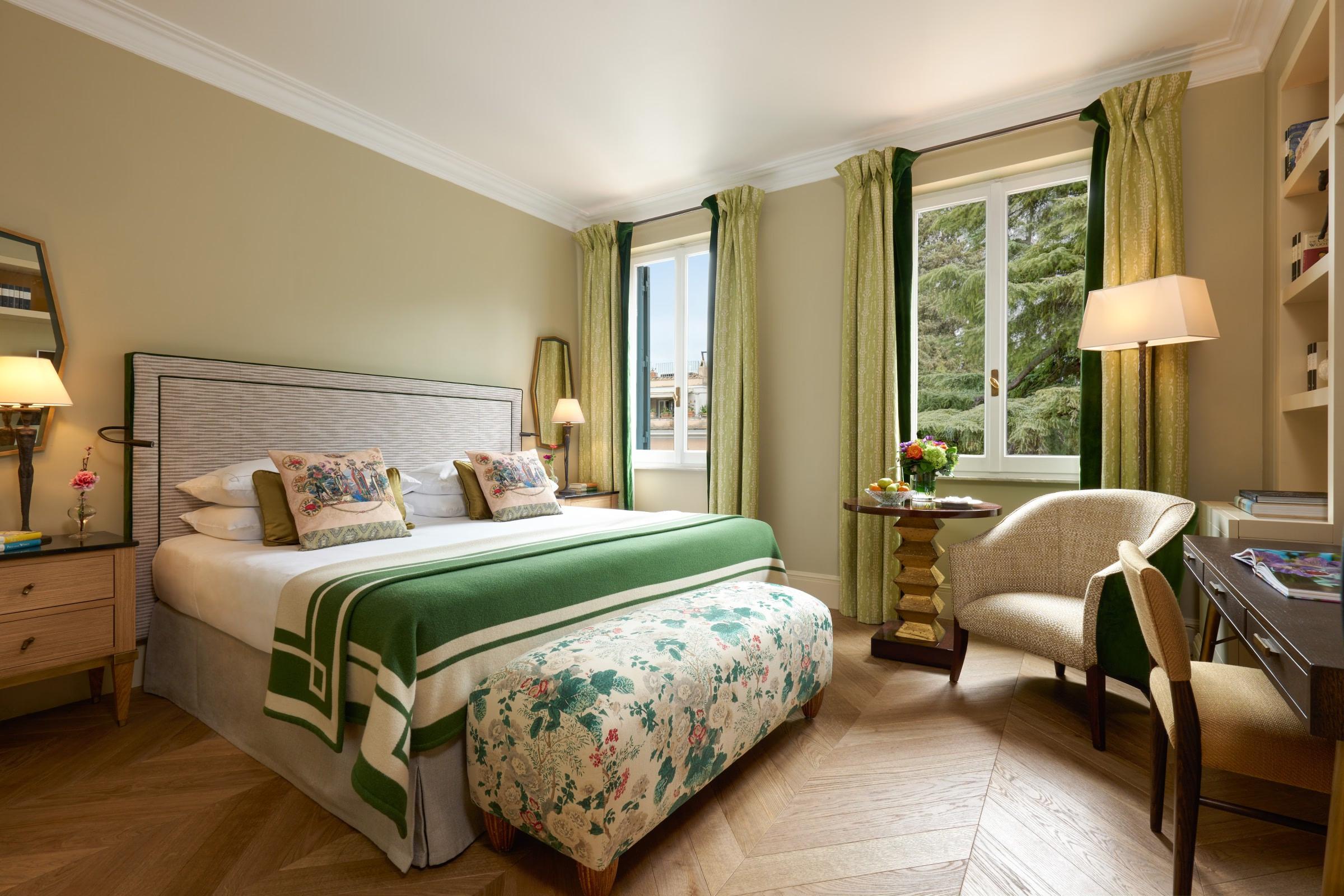 Bedroom with green headboard, patterned fabrics, and seating by window with garden view