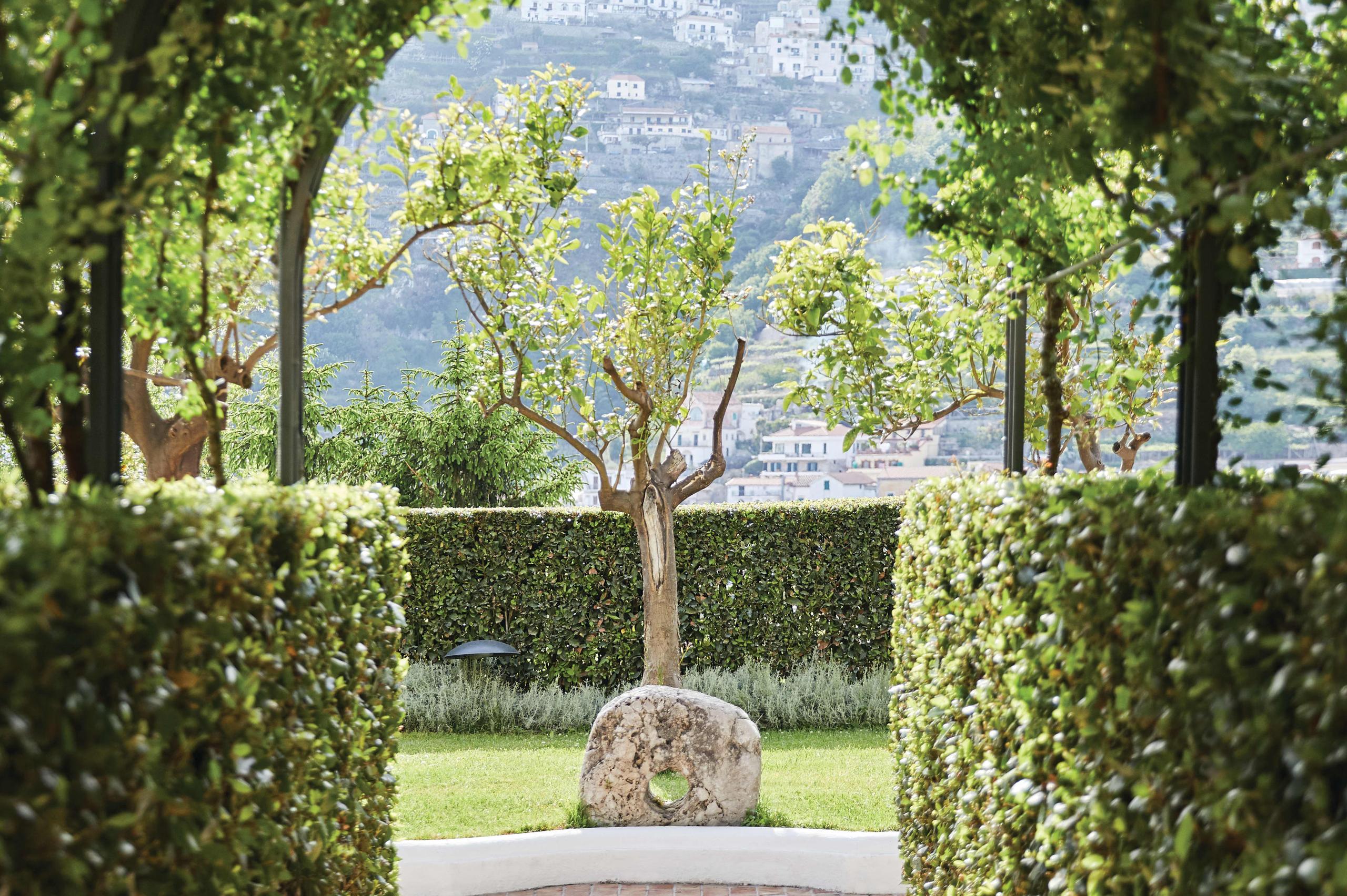 Caruso: garden corridor framed by trimmed hedges with lawn and scenic coastal vista beyond
