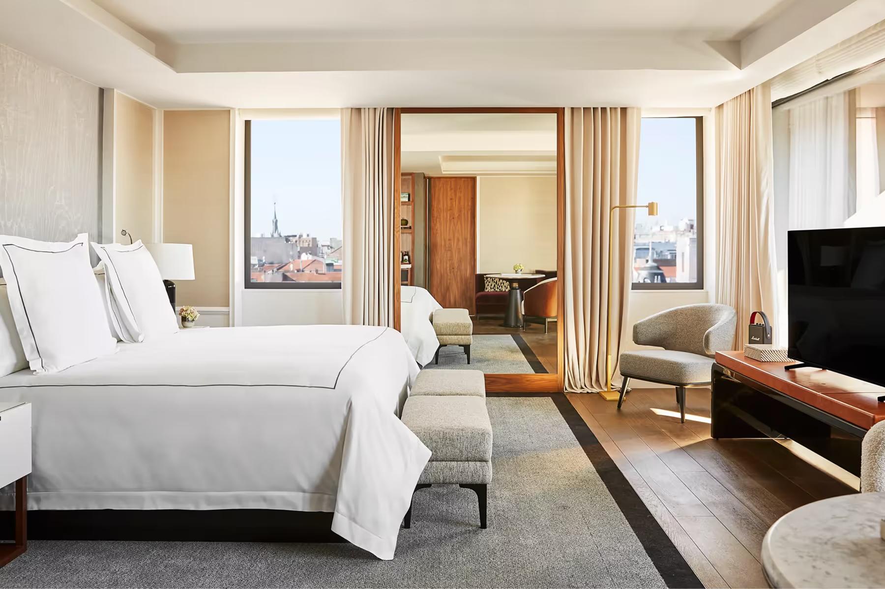 Rosewood Villa Magna: a guest room with white bedding, floor-to-ceiling windows with city views, and warm wood accents