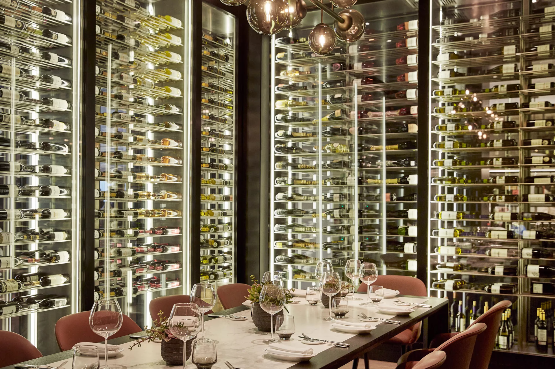 A private dining room with wine bottles wall-mounted behind glass, white tablecloths, and formal service